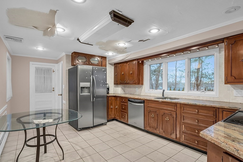 Kitchen with dark wood cabinets, stainless steel appliances, and extensive ceiling damage.
