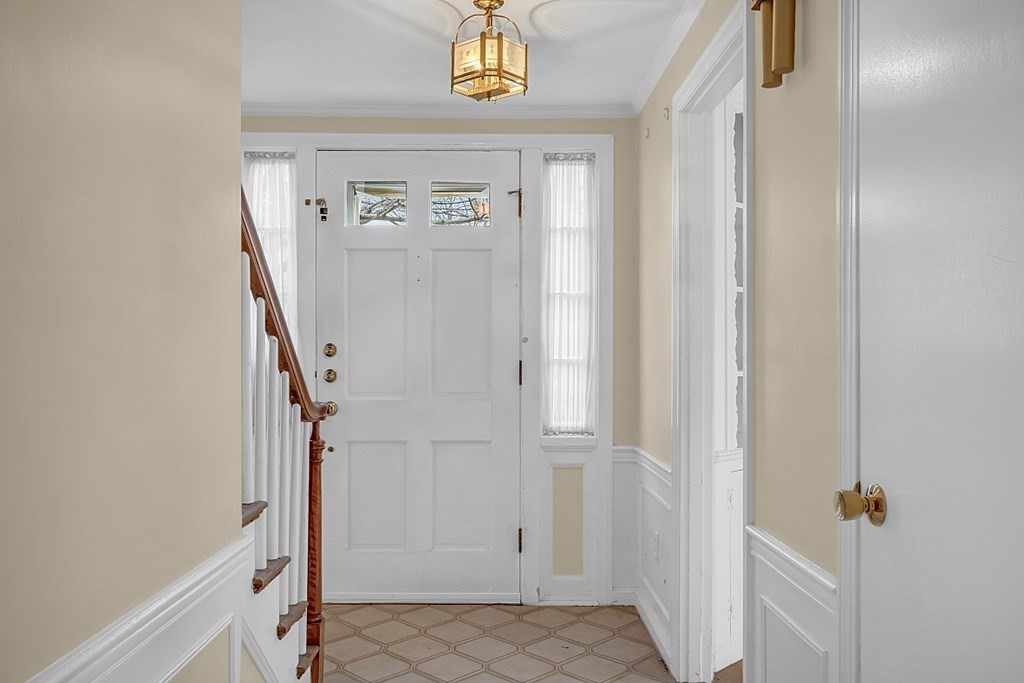 Entry foyer with a white double door, patterned tile floor, and staircase with a wooden handrail.