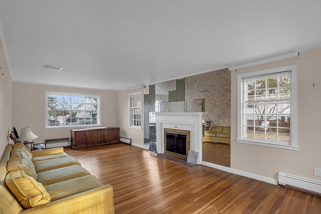 Living room with hardwood floors, a white fireplace, mirrored panels, and a yellow sofa.