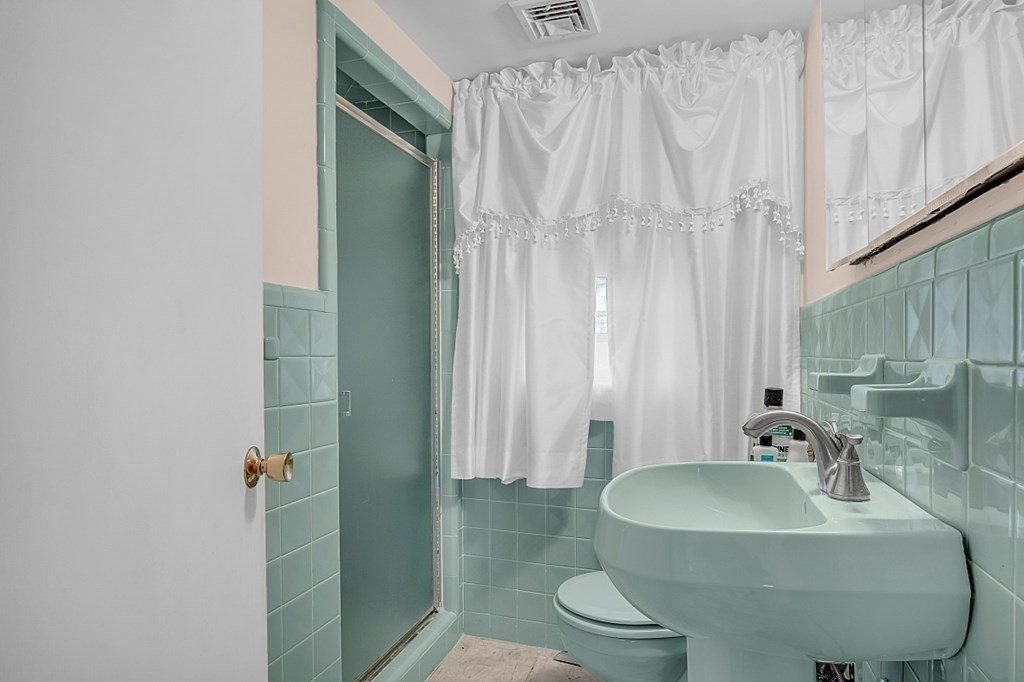 Bathroom with mint-green tile, a curtained shower, and a large white sink.