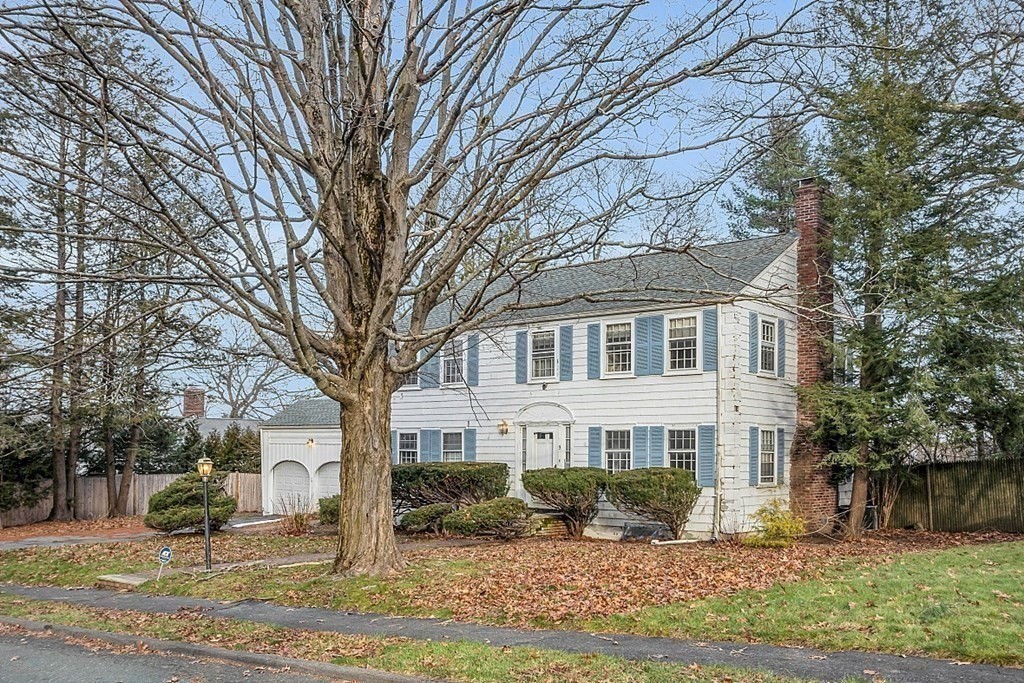 White two-story house with blue shutters, an attached garage, and a large leafless tree in the yard.