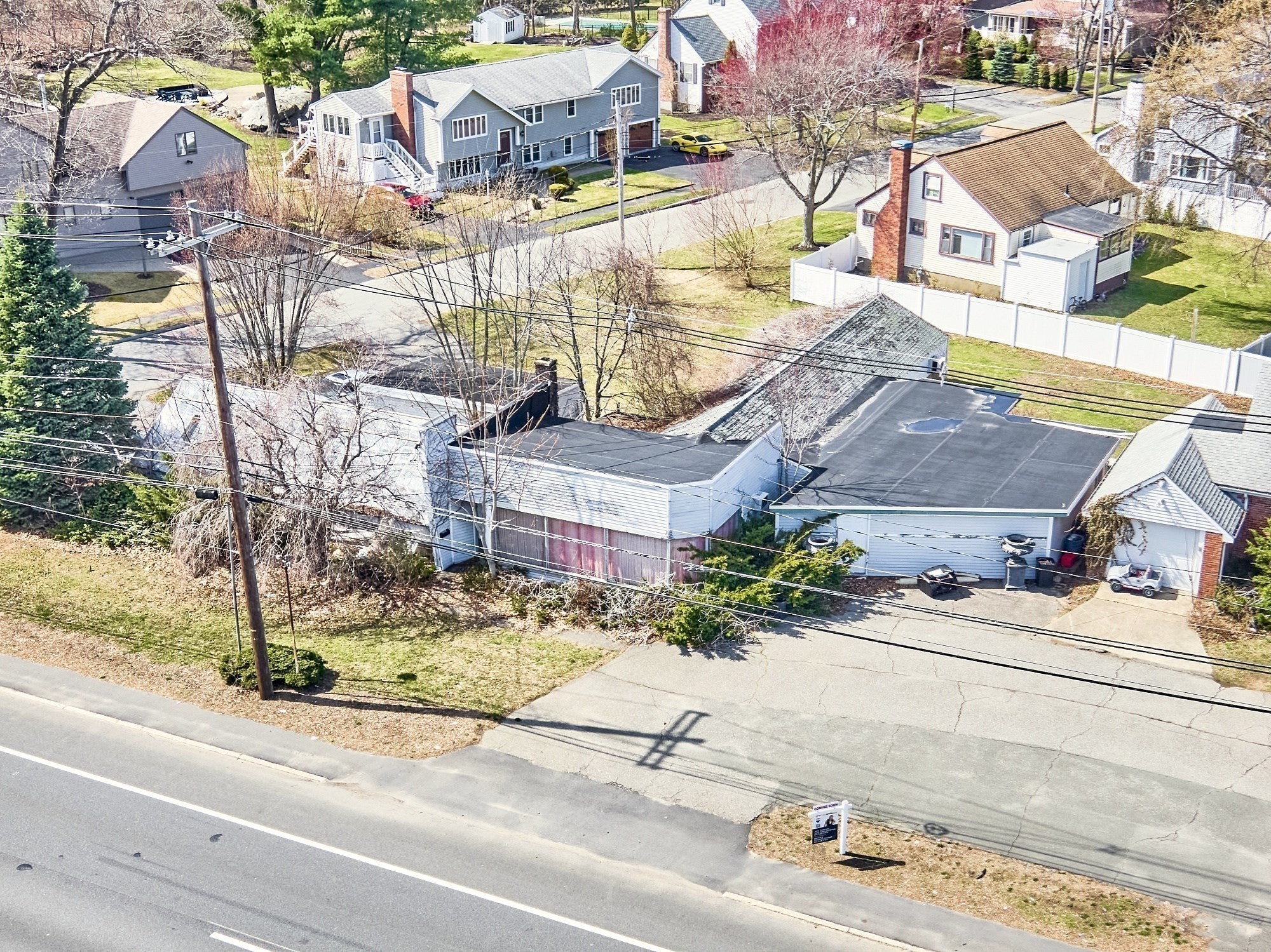 Aerial view of the white commercial building beside the road, with neighboring homes and utility lines.
