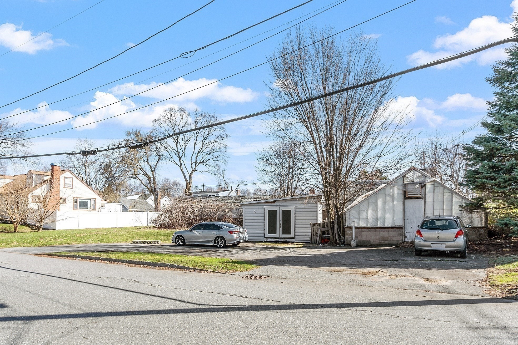Property exterior with a gray outbuilding, greenhouse, and paved parking area.