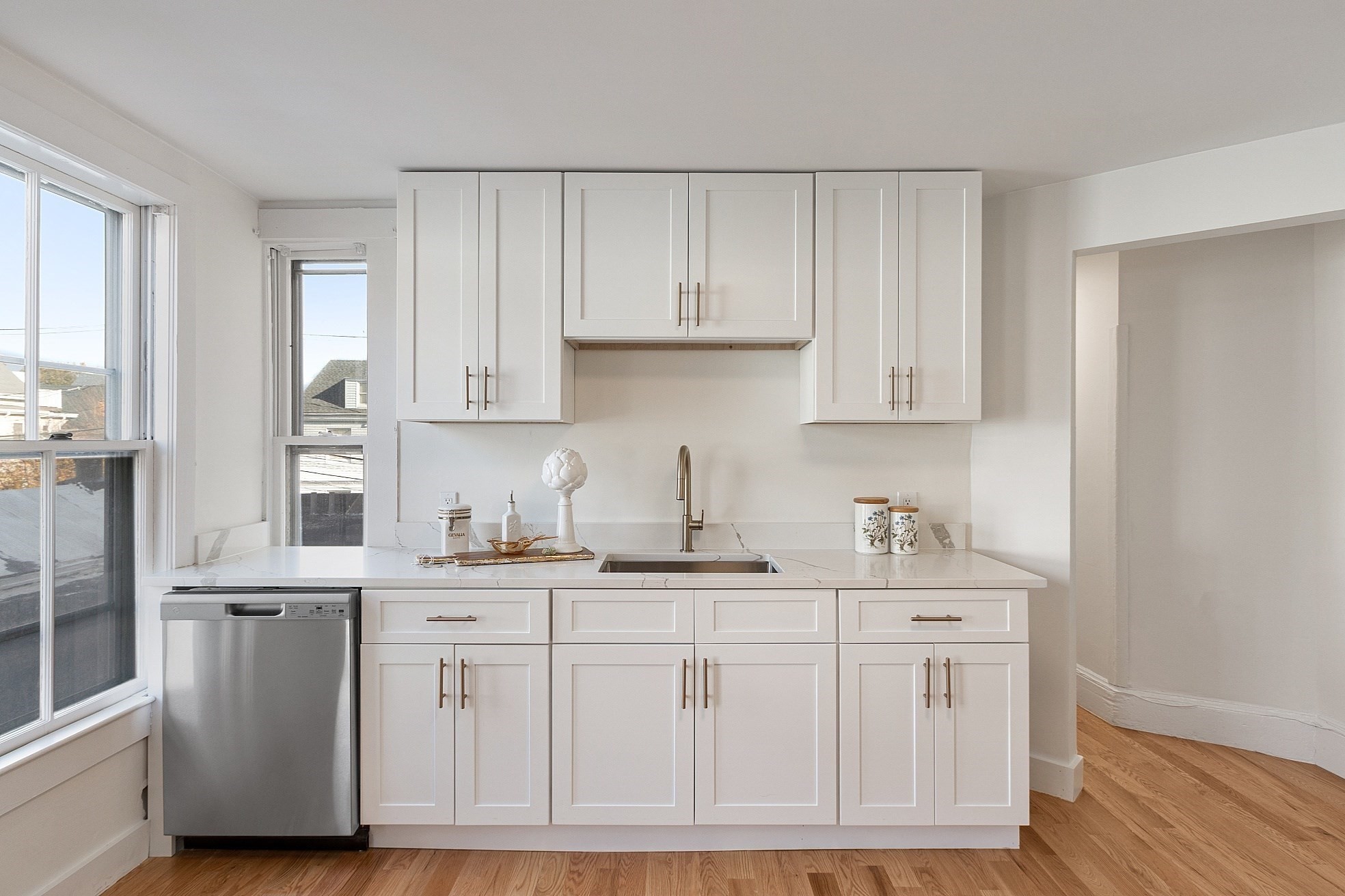 Bright white kitchen with shaker cabinets, veined countertops, and a stainless steel dishwasher.