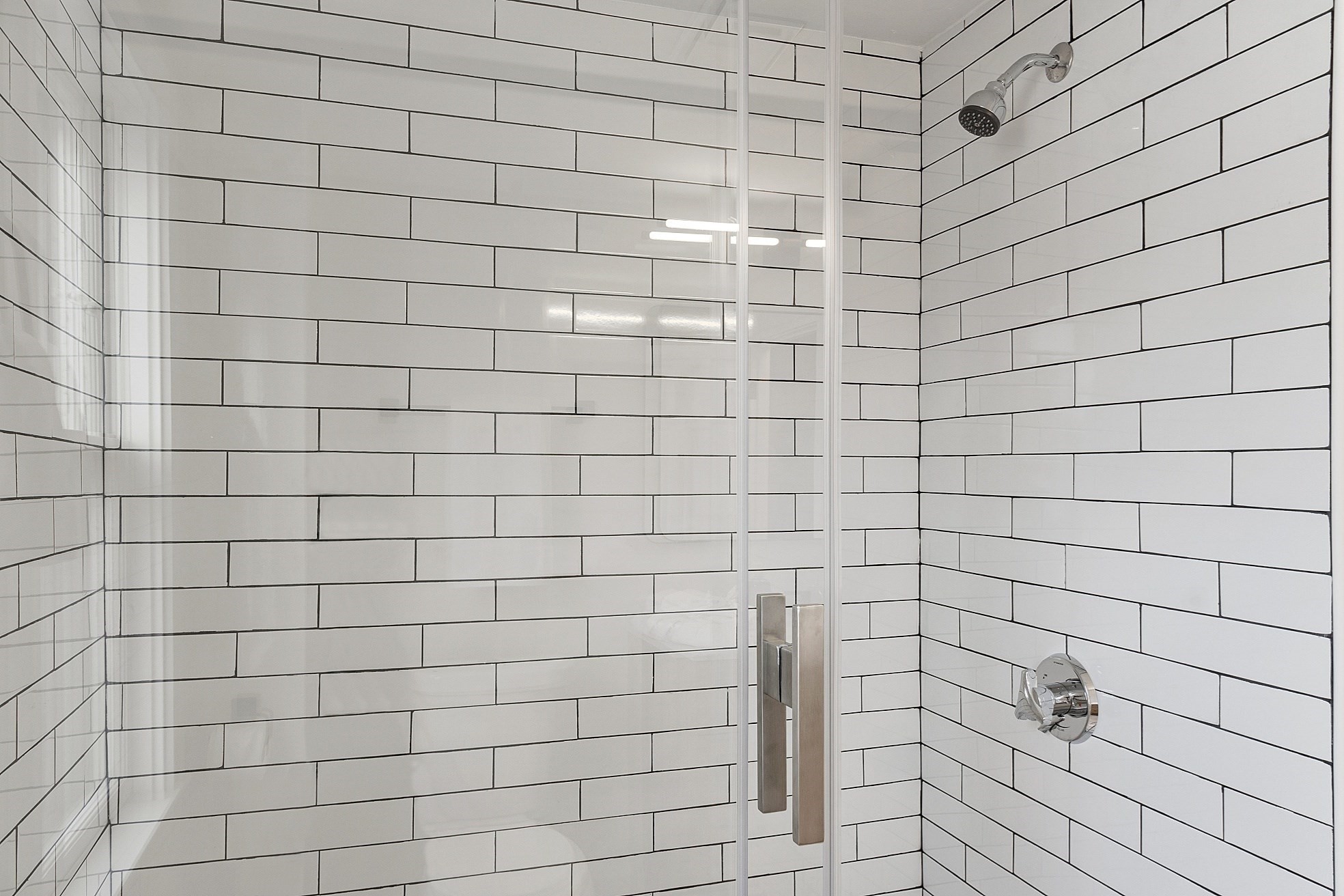 Tiled shower with a clear glass enclosure and chrome fixtures.