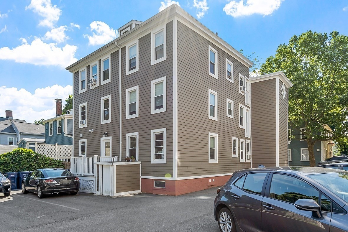 Multi-story gray residential building with white trim and parked cars in the lot.