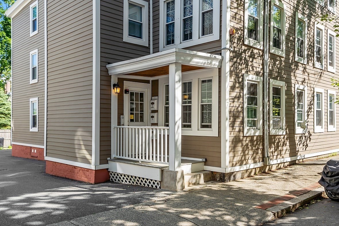 Multi-unit building entrance with tan siding, white trim, and a covered porch.