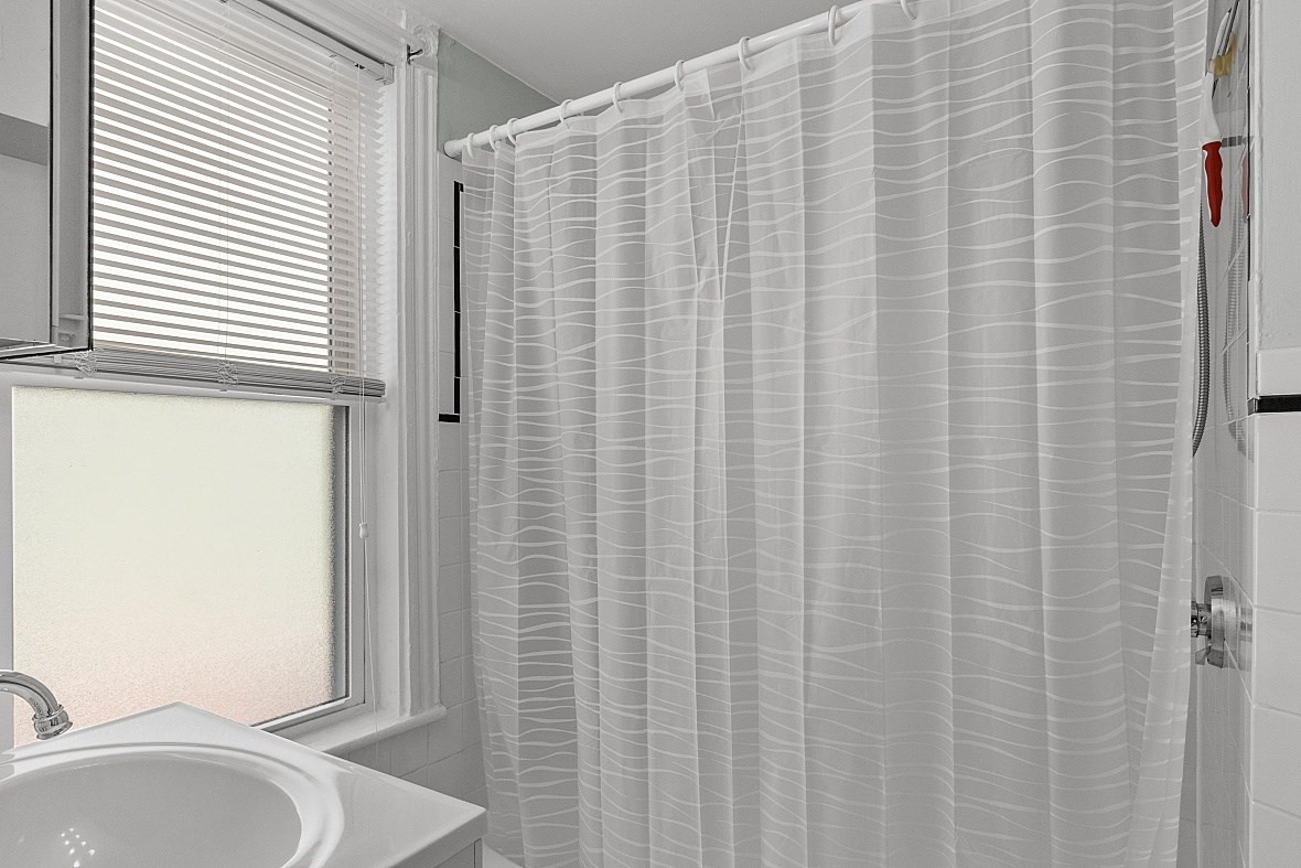 Bathroom with a white shower curtain, sink, and frosted window.