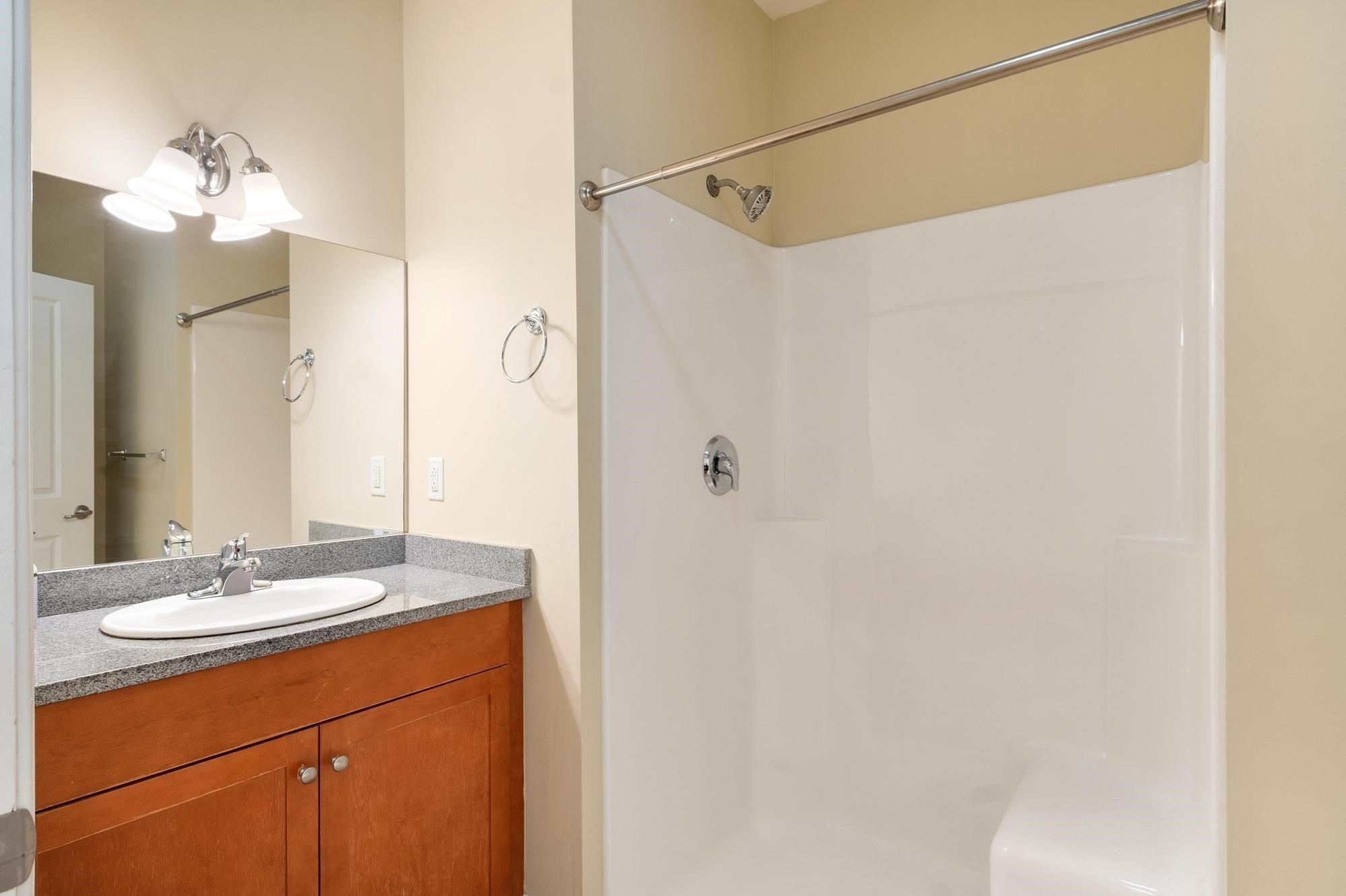 Bathroom with a white tub and shower beside a wood vanity with a gray countertop.