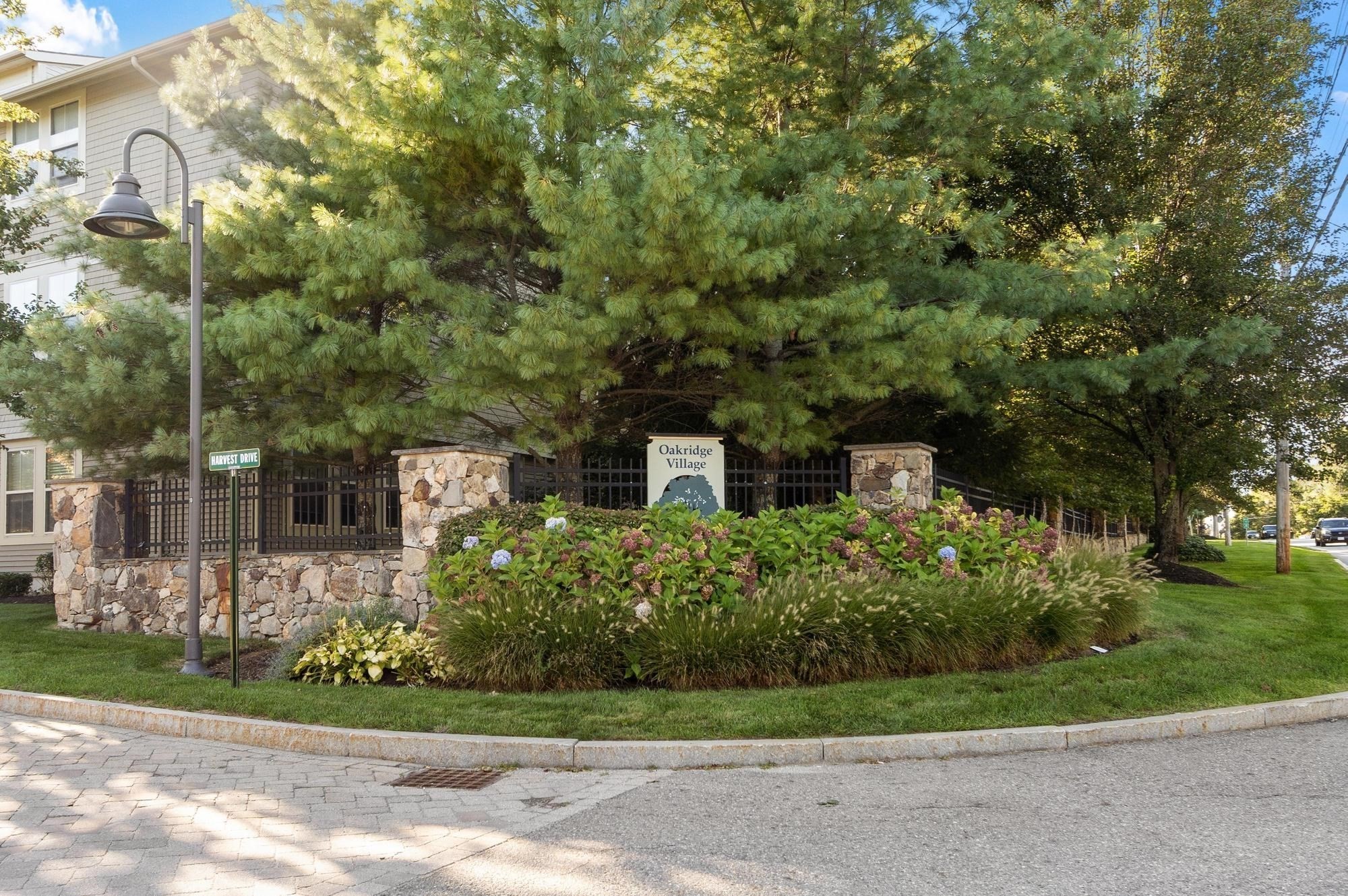 Oakridge Village entrance sign among flowering shrubs, stone pillars, and mature pine trees.