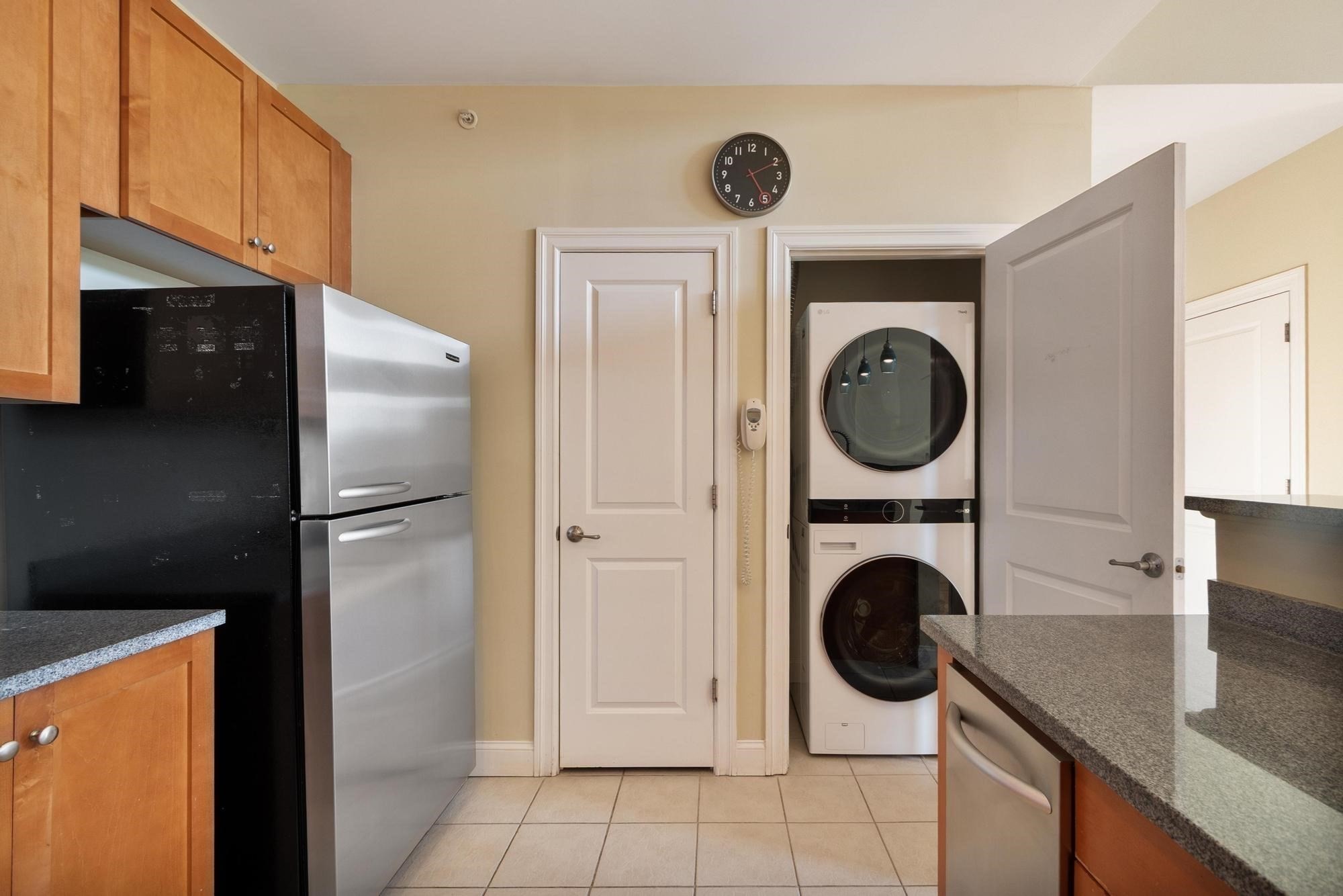 Kitchen with wood cabinets, granite counters, and a stacked washer and dryer behind an open door.