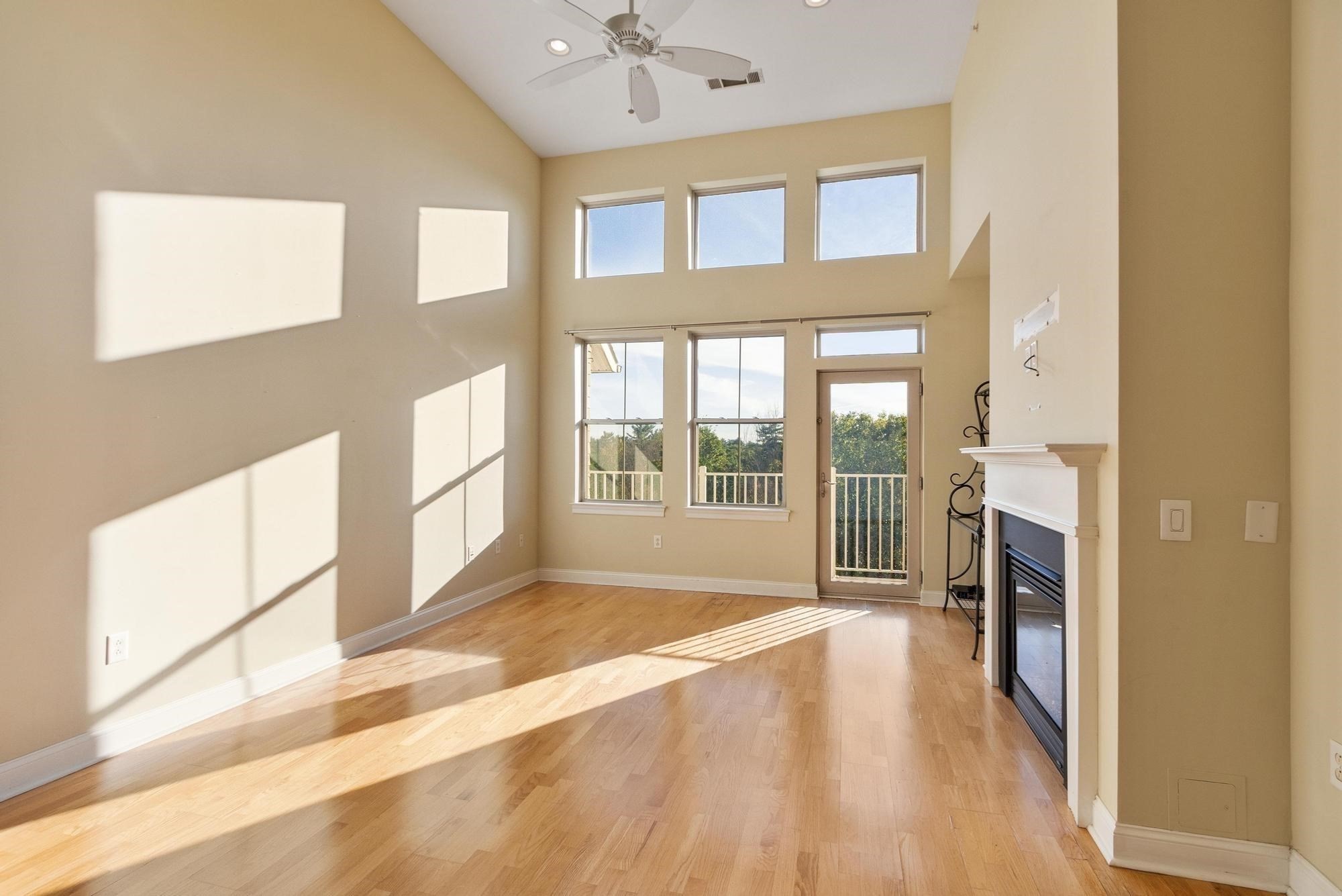 Empty living room with hardwood floors, tall windows, vaulted ceiling, and fireplace.