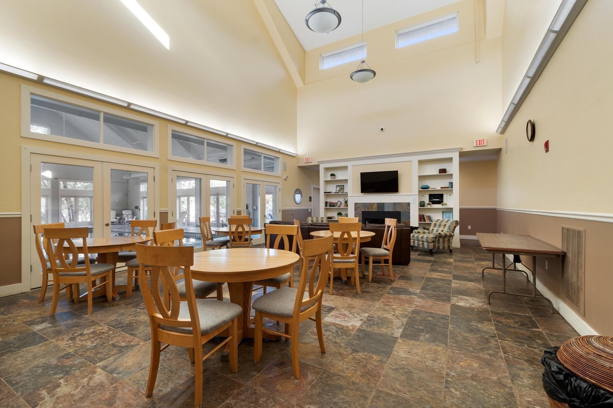 Communal lounge and dining room with wooden tables, a fireplace, and built-in shelving.