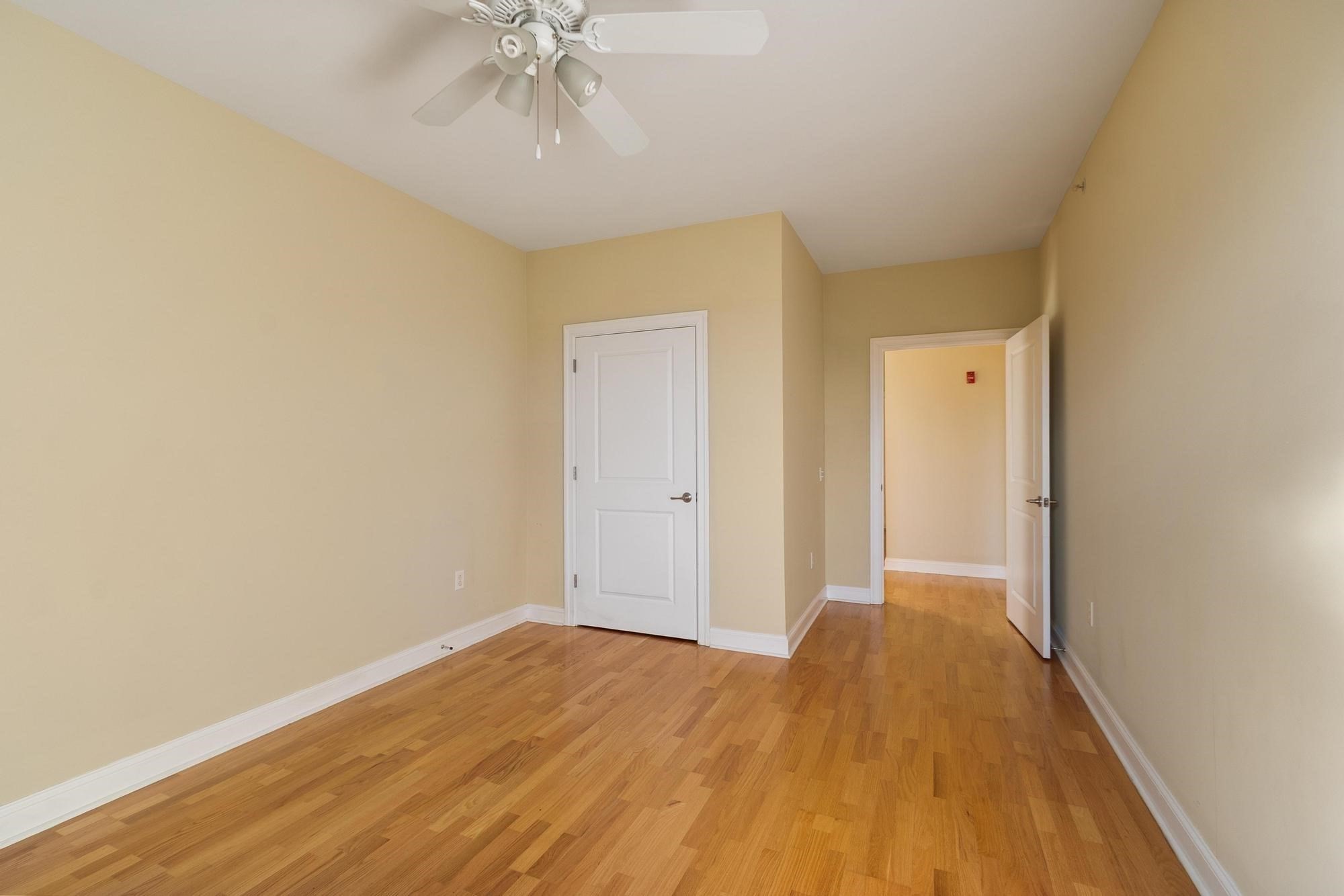 Empty room with hardwood floors, a ceiling fan, and an open doorway to the hall.