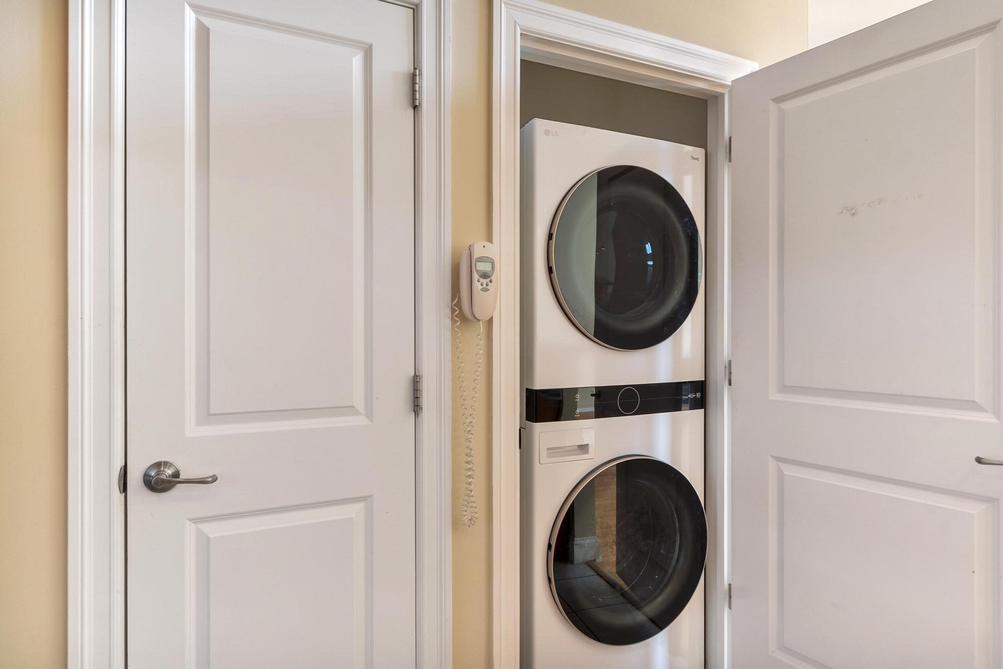 Stacked front-loading washer and dryer in a closet beside white paneled doors.