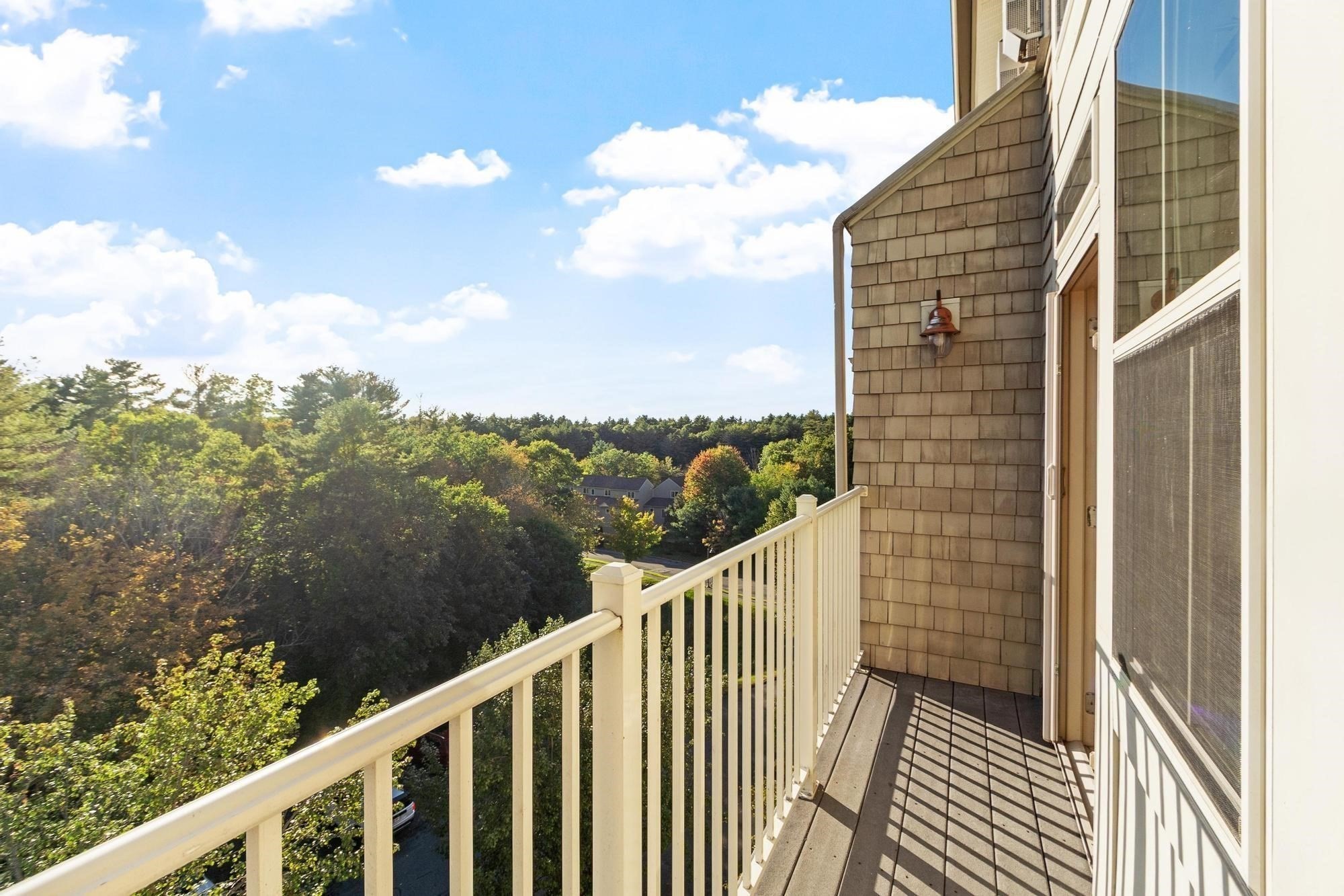 Upper-level balcony overlooking trees and neighboring homes, with brown shingle siding and a cream railing.