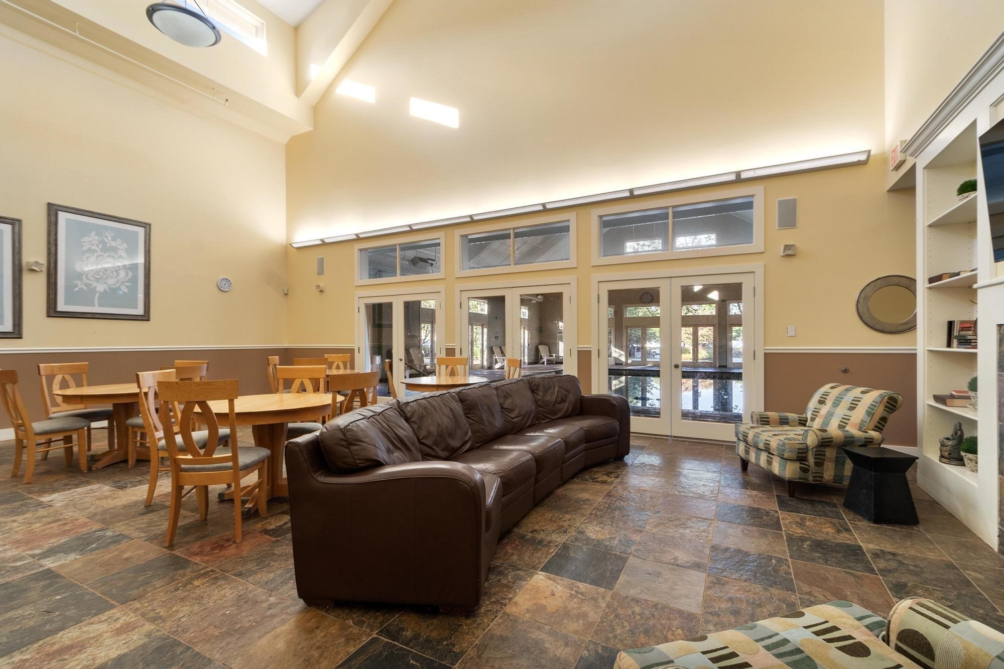 Communal lounge and dining area with a leather sofa, wooden tables, and tall glass doors.