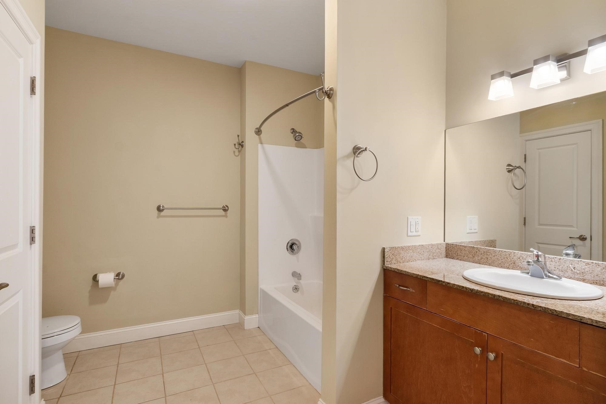 Bathroom with a tub and shower, granite-topped wood vanity, large mirror, and partly visible toilet.