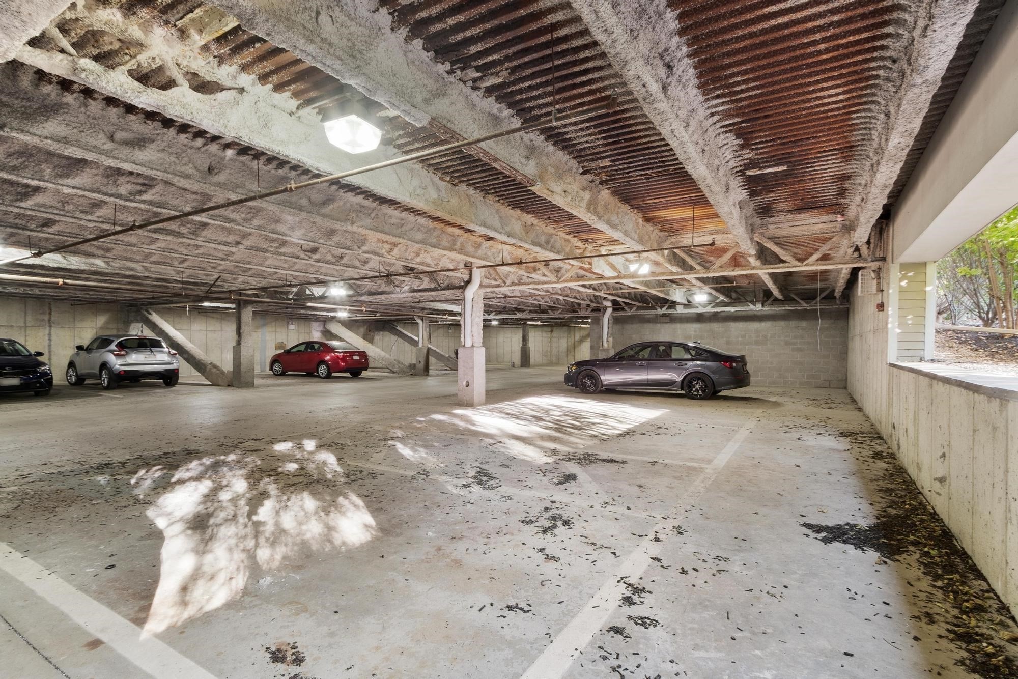Concrete parking garage with marked spaces, several cars, and an open side facing trees.