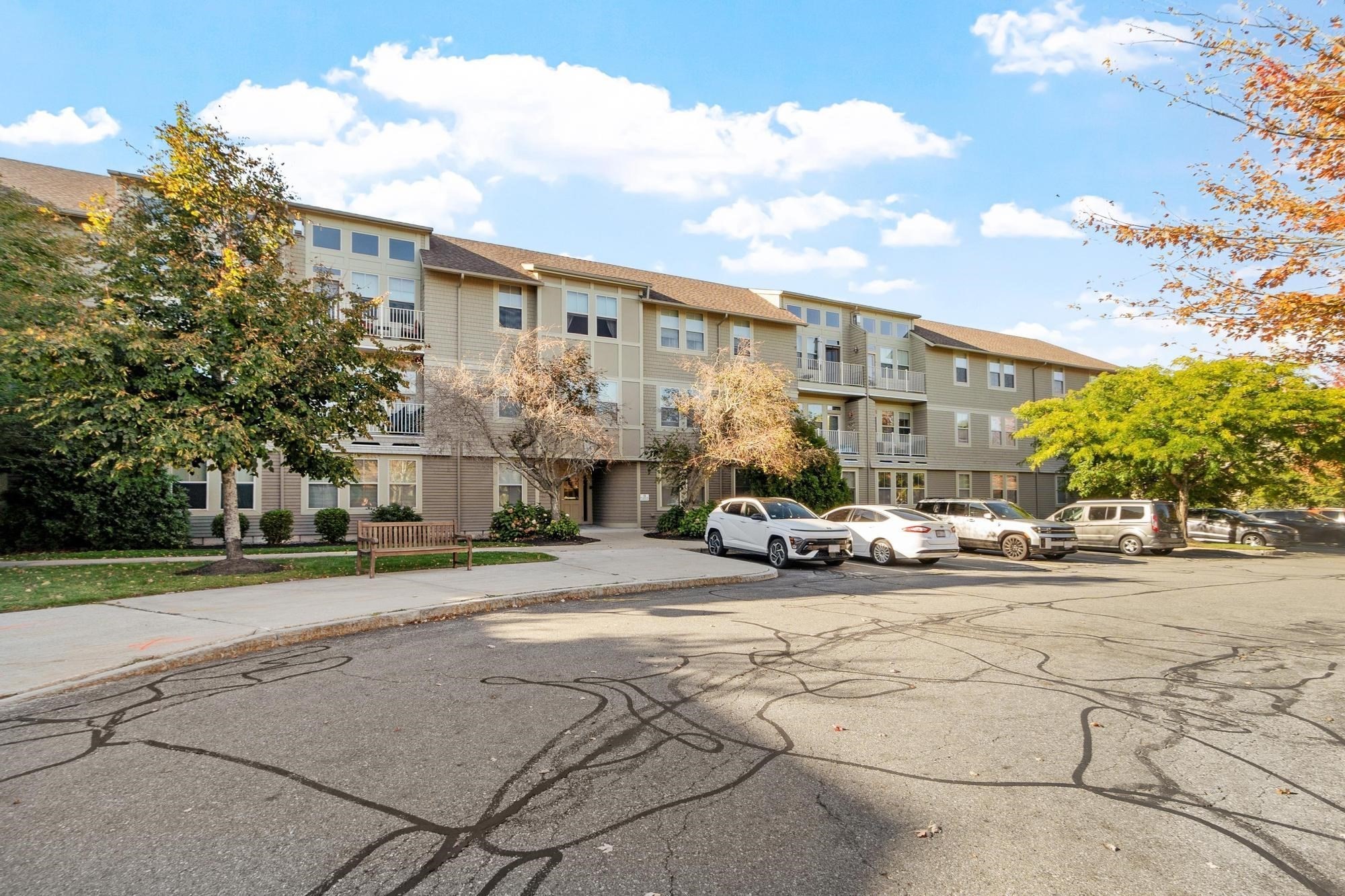 Multi-story condominium building with balconies, parked cars, and trees along the front.