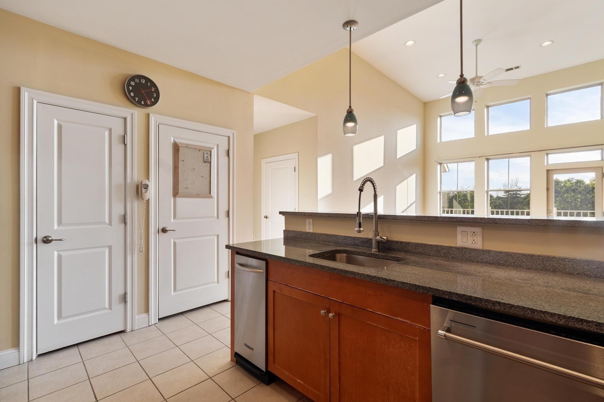 Kitchen with granite counters, reddish wood cabinets, stainless steel appliances, and a vaulted ceiling with tall windows.