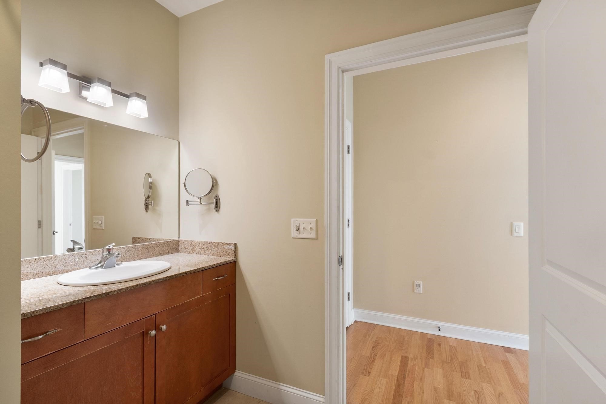 Bathroom vanity with a stone countertop and oval sink beside an open doorway to a hardwood-floored room.