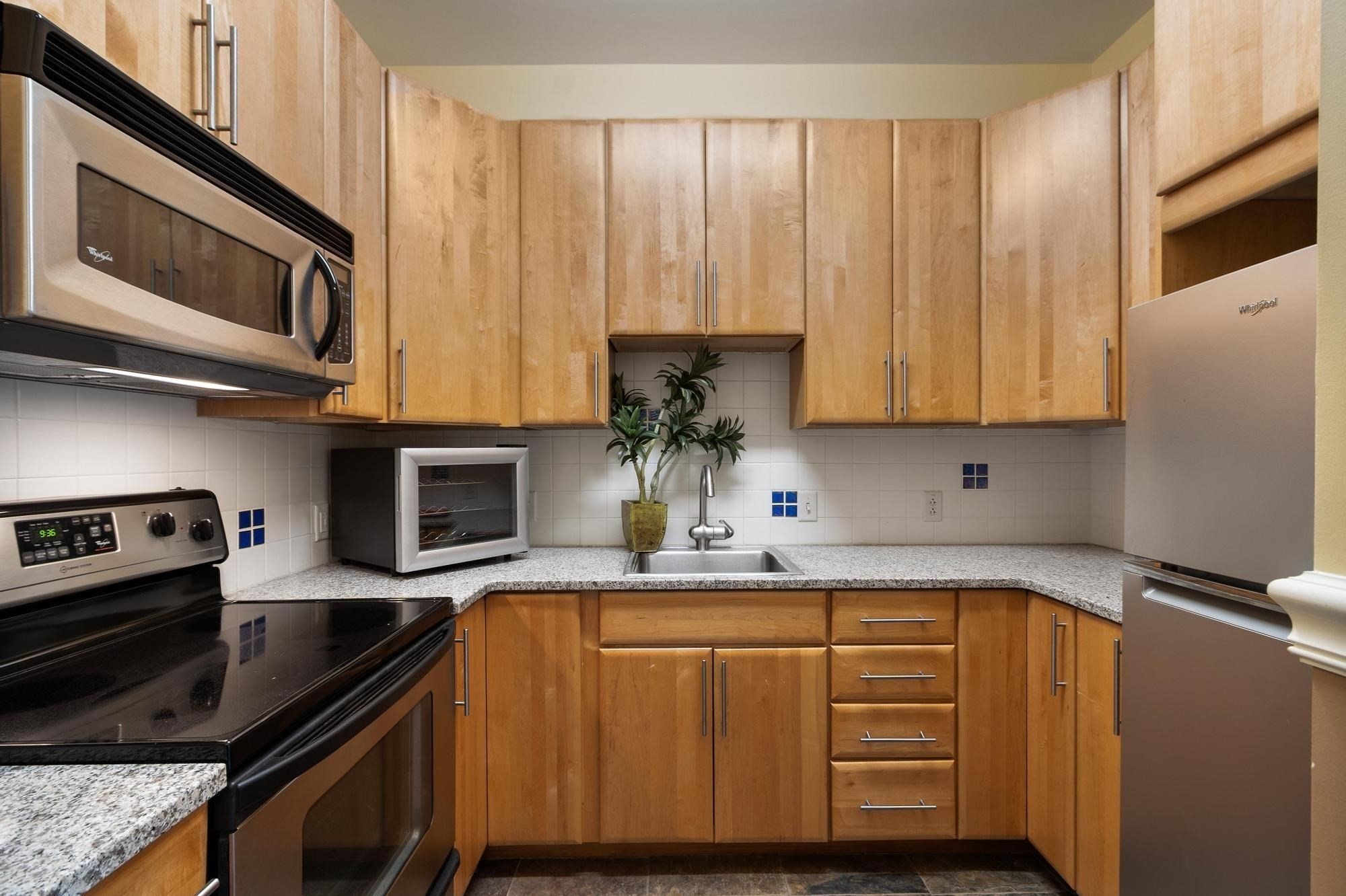 Kitchen with honey-colored wood cabinets, granite counters, stainless steel appliances, and blue accent tiles.