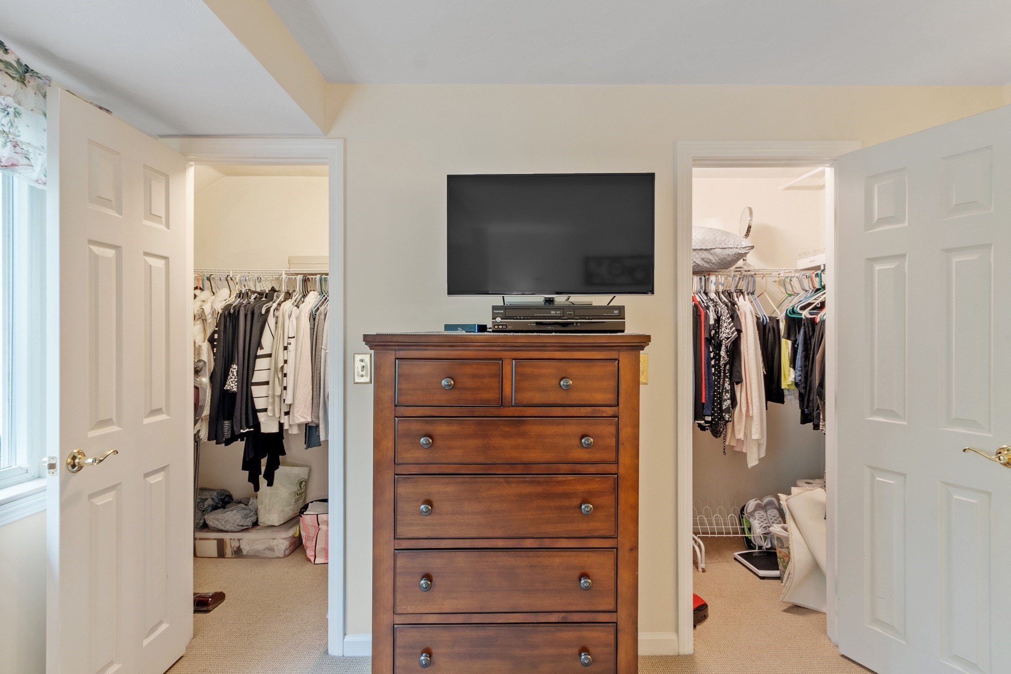 Bedroom with a wooden dresser and television between two open walk-in closets