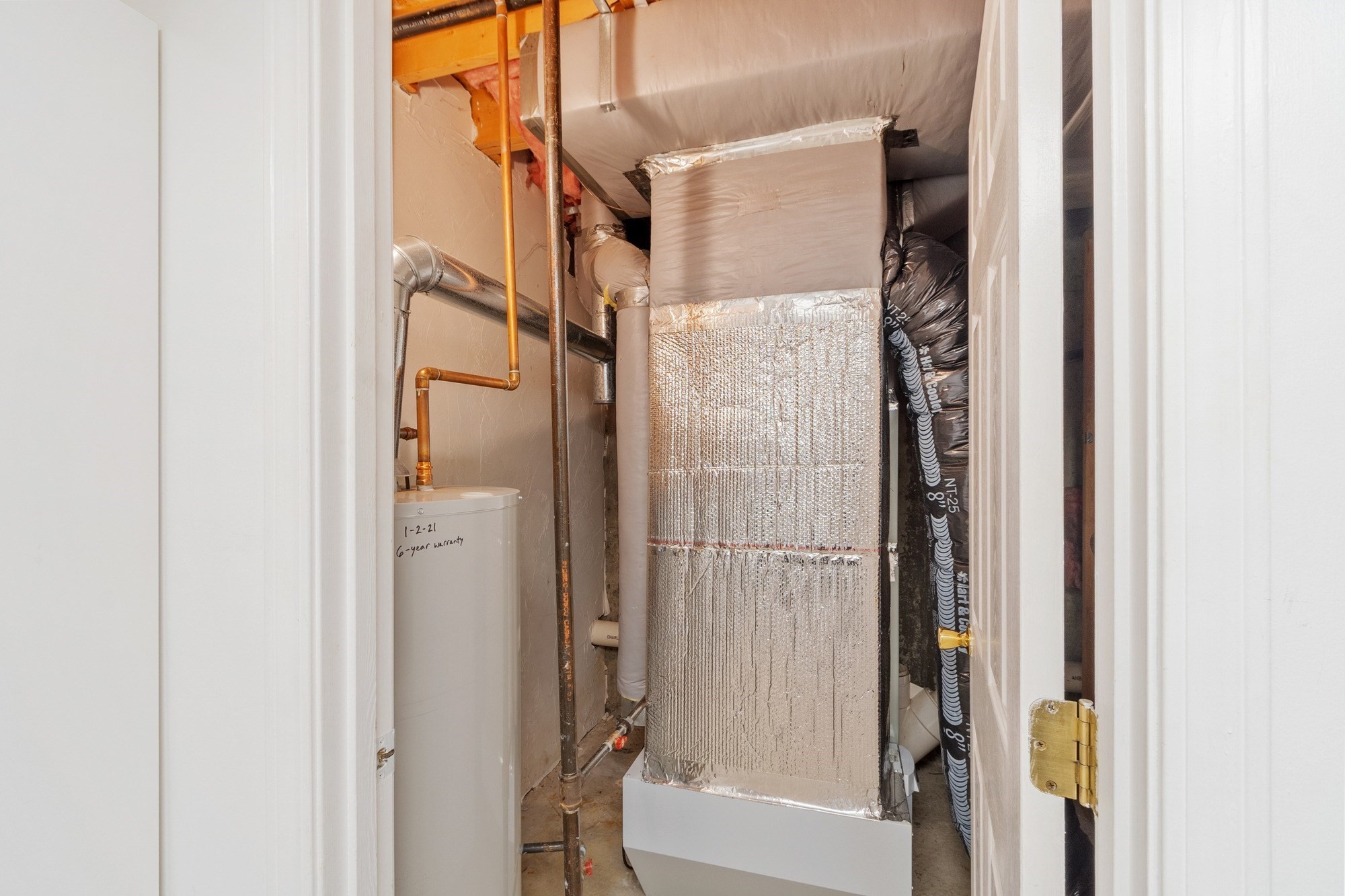 Utility closet with a foil-wrapped HVAC furnace, exposed pipes, and a water heater.