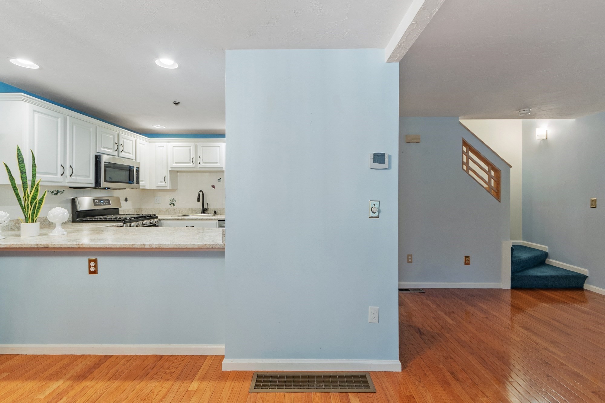 Kitchen and adjoining stairway with white cabinets, blue walls, and hardwood floors.