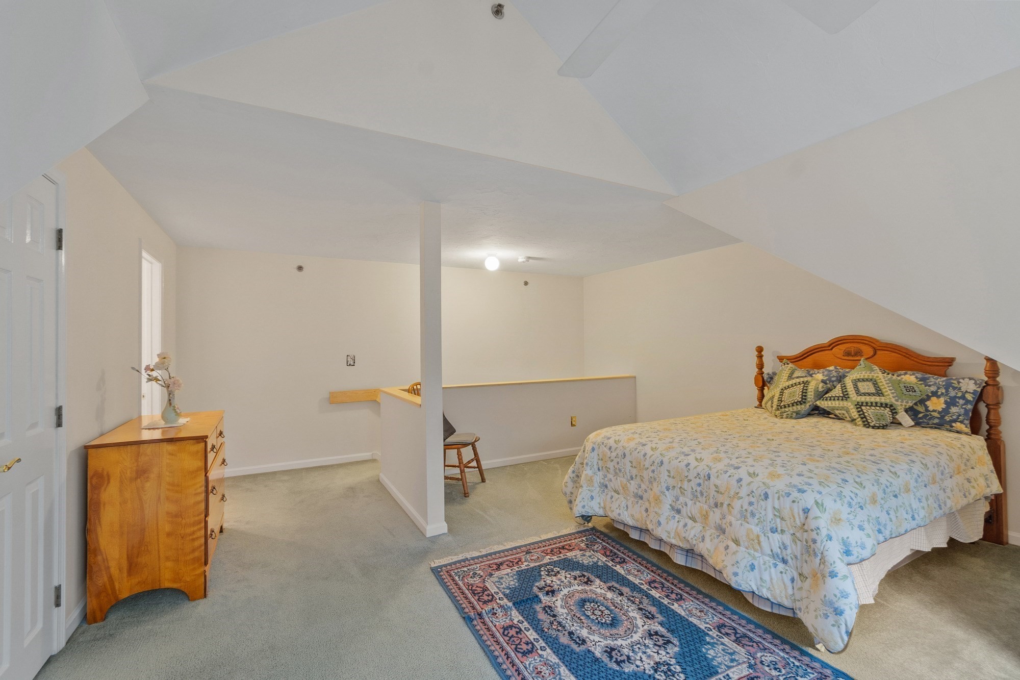 Furnished bedroom with a wooden bed and floral bedding beneath a sloped ceiling.
