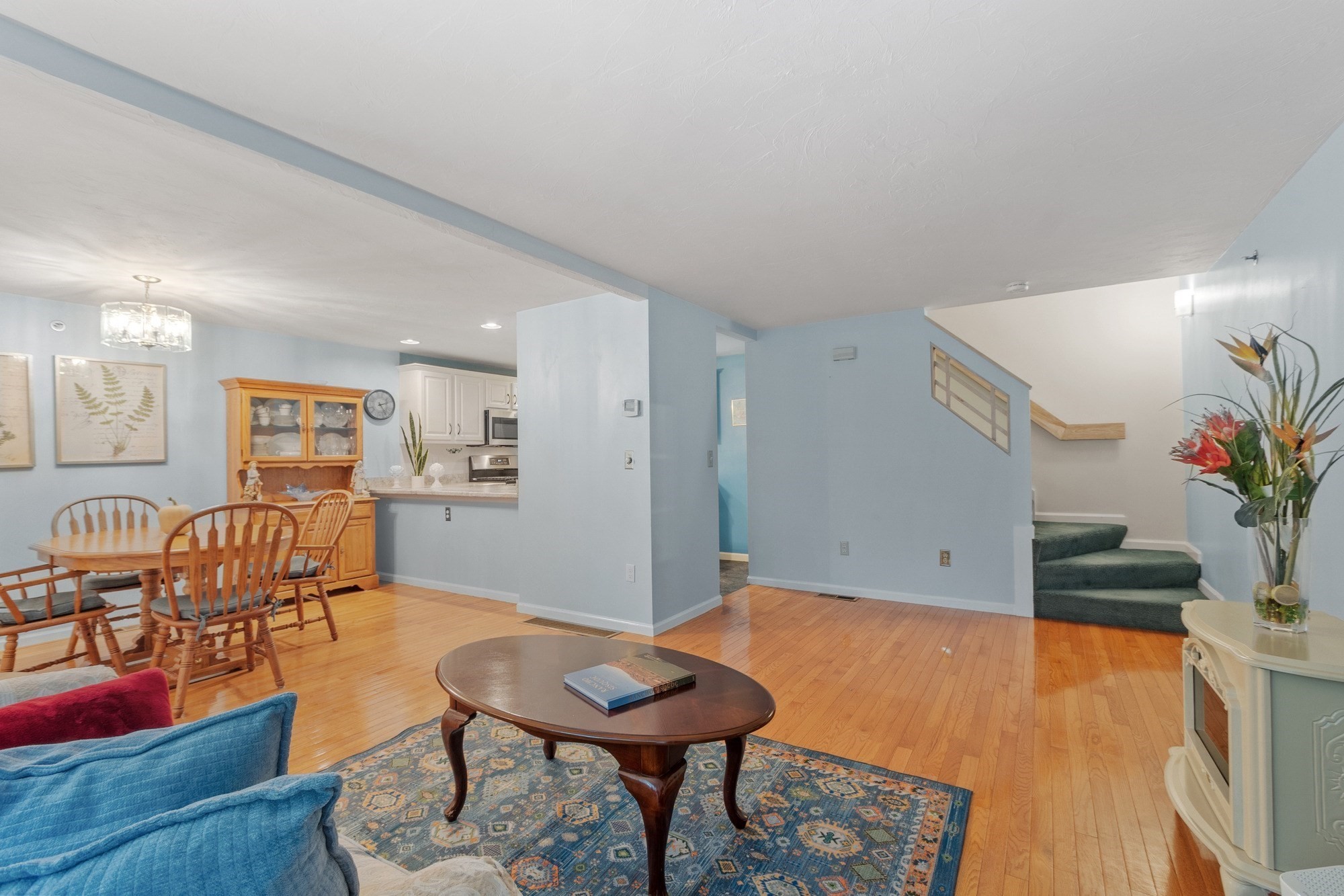 Open-plan living and dining area with blue seating, hardwood floors, and carpeted stairs.