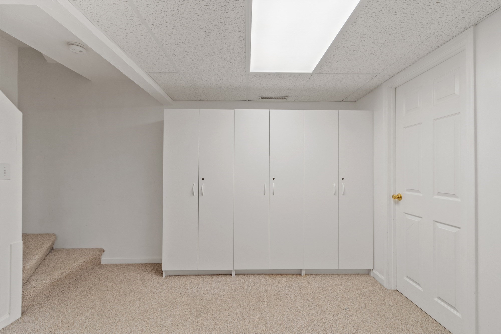 Carpeted storage area with white cabinets, a paneled door, and stairs.