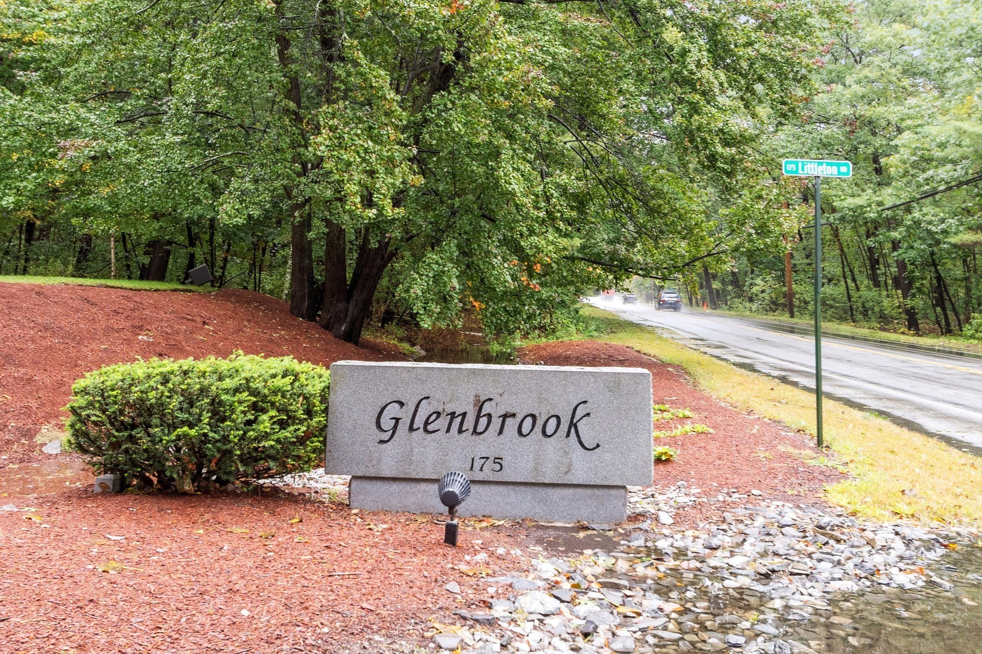Glenbrook entrance sign beside a wet, tree-lined road.