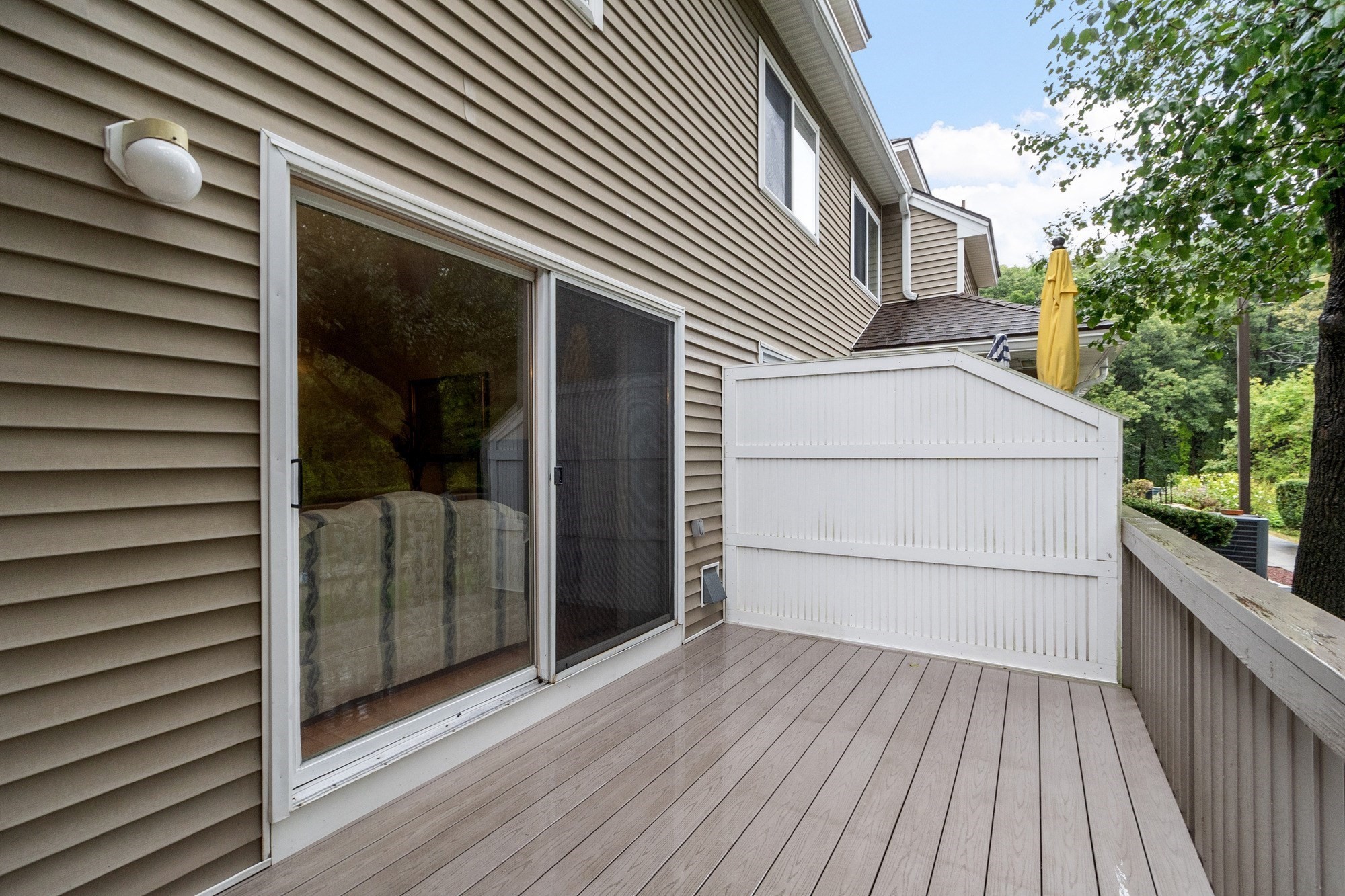 Raised deck with composite flooring, white privacy partition, and sliding glass door.