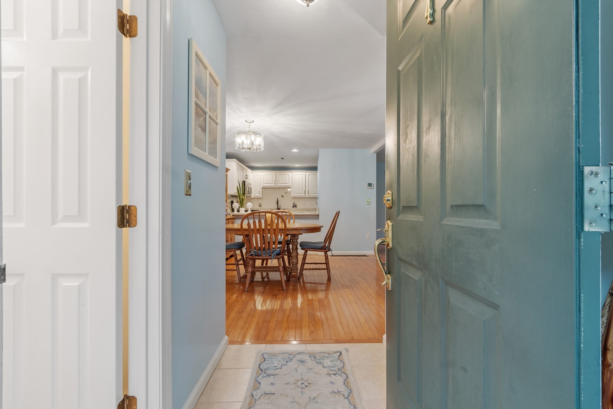 Open teal entry door overlooking a hardwood dining area and white-cabinet kitchen.