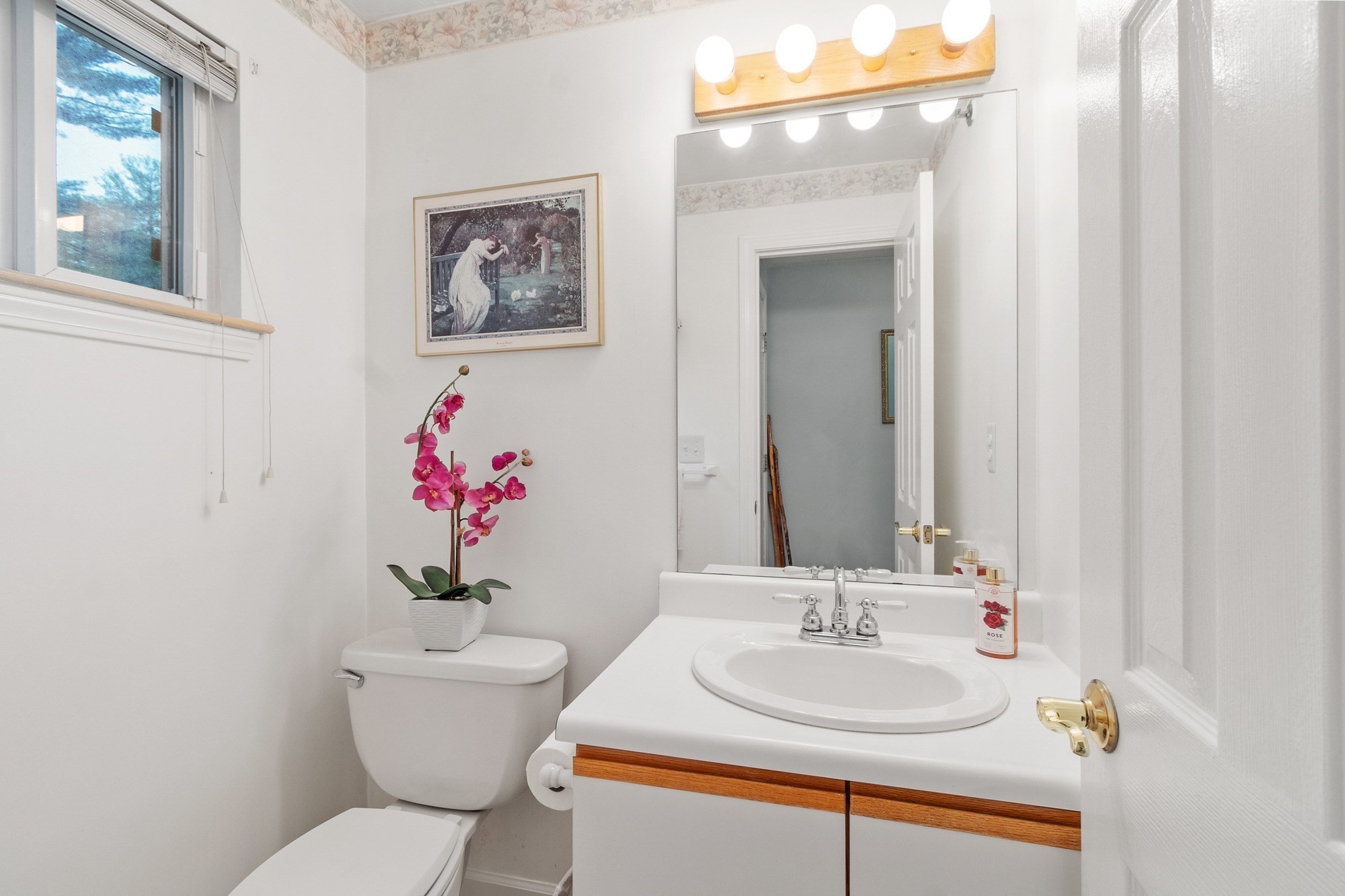 Bathroom with a white vanity and large mirror, toilet, window, and pink orchid.