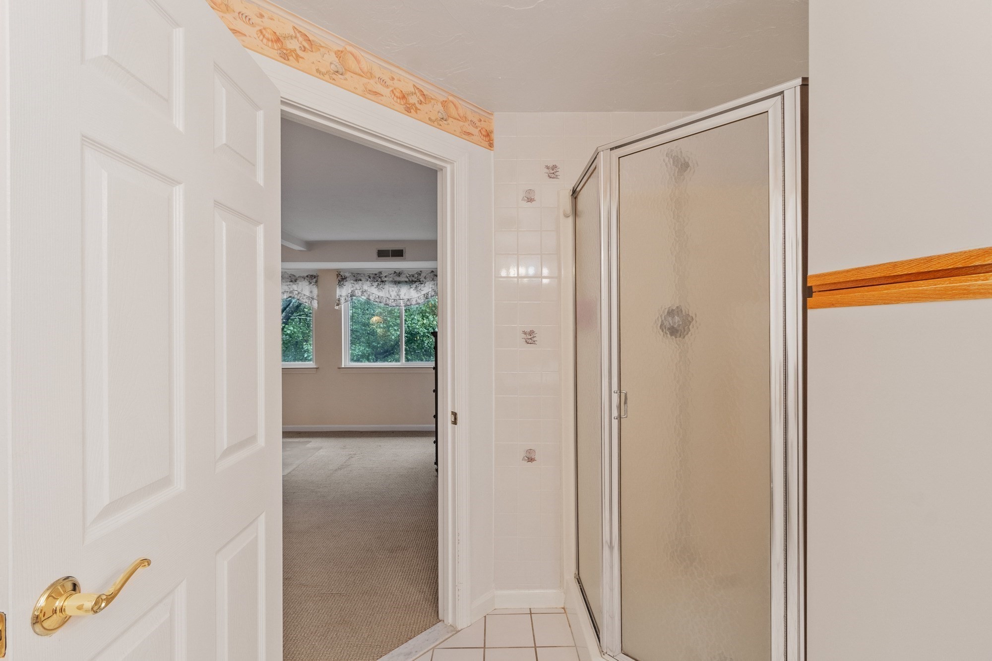 Bathroom with a glass-enclosed shower and an open doorway to a carpeted room.