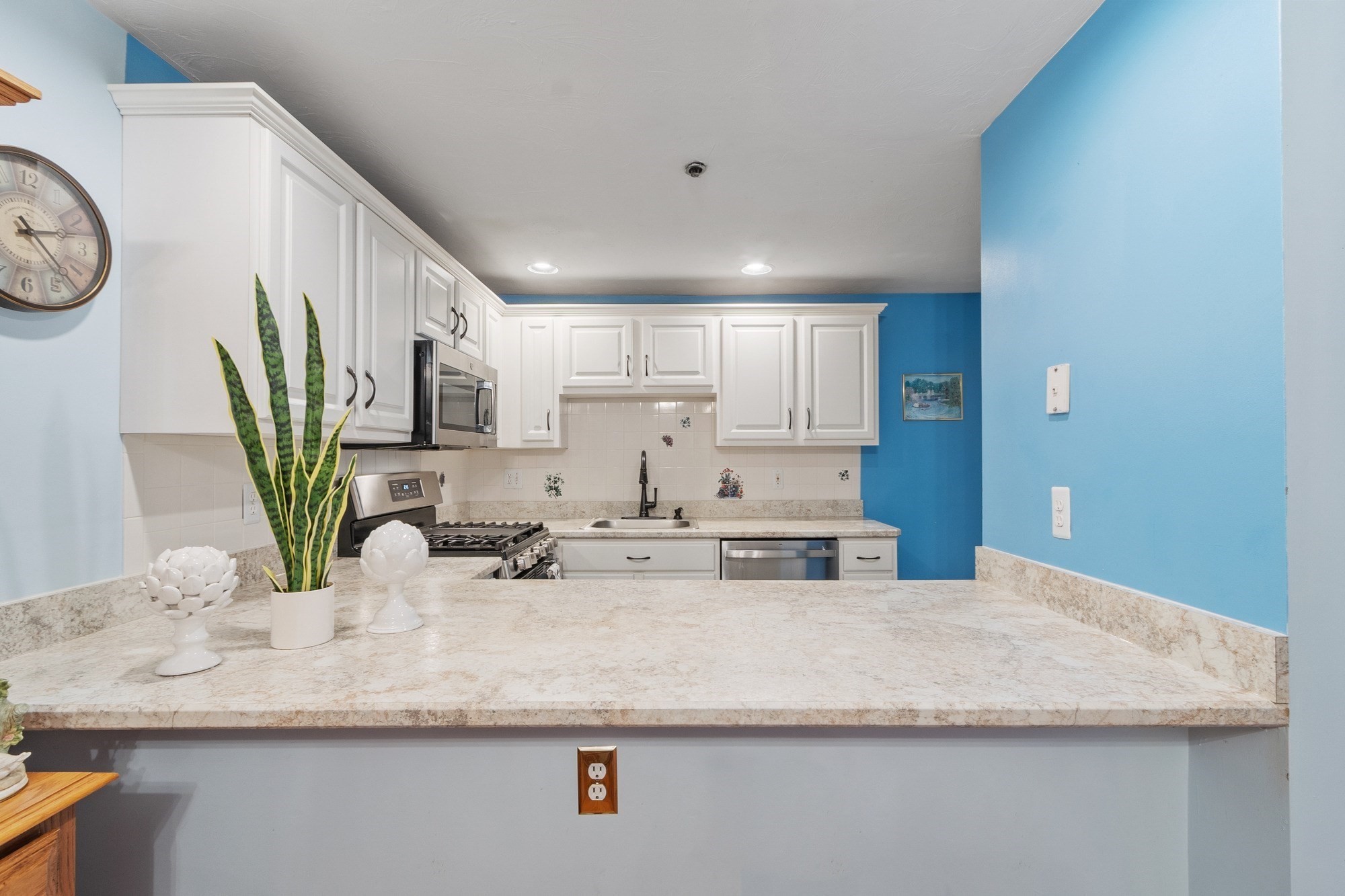 Kitchen with white cabinets, stainless appliances, blue walls, and a broad stone breakfast bar.