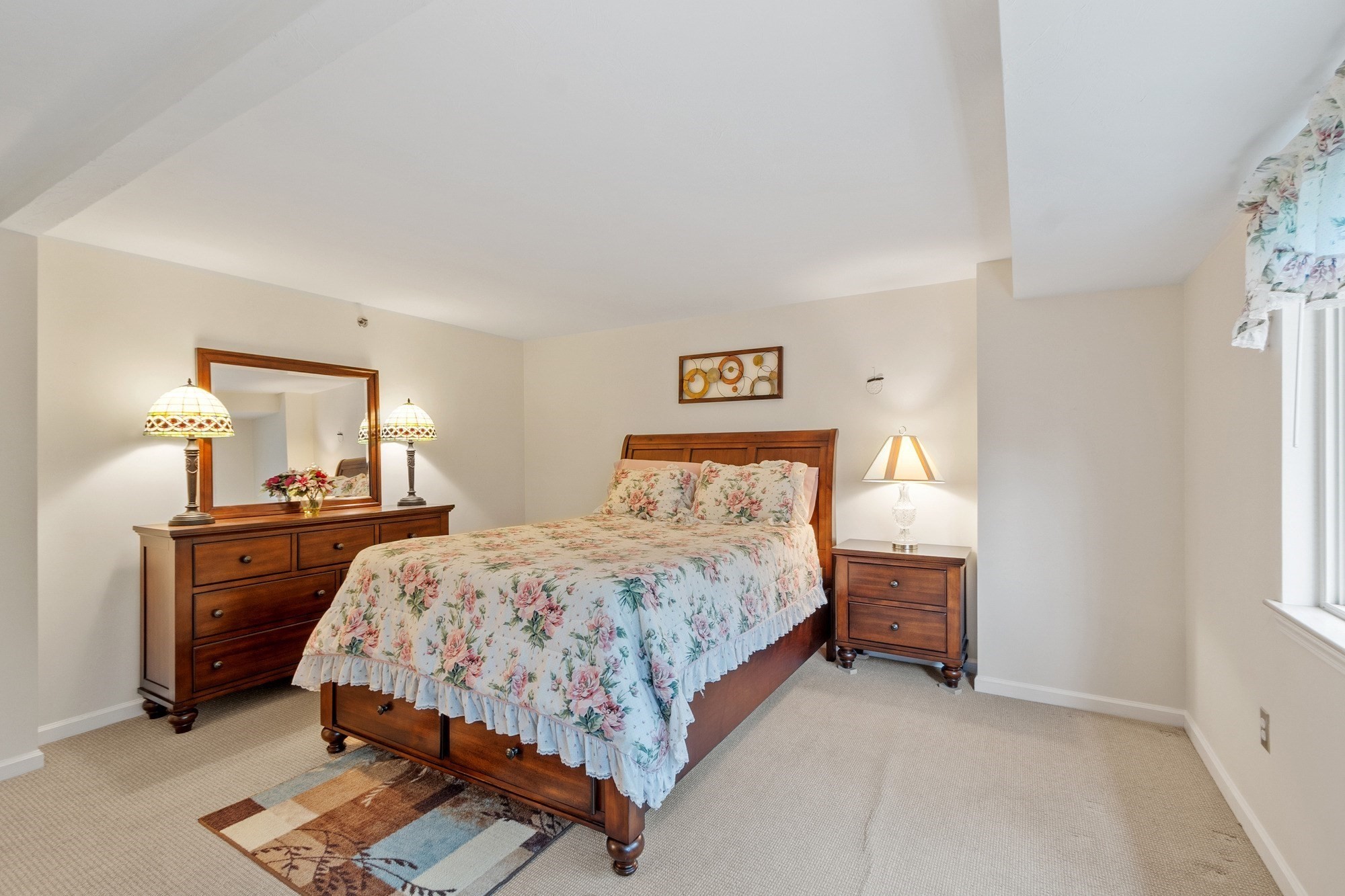 Bedroom with a wooden bed, floral bedding, matching dresser, and mirror.