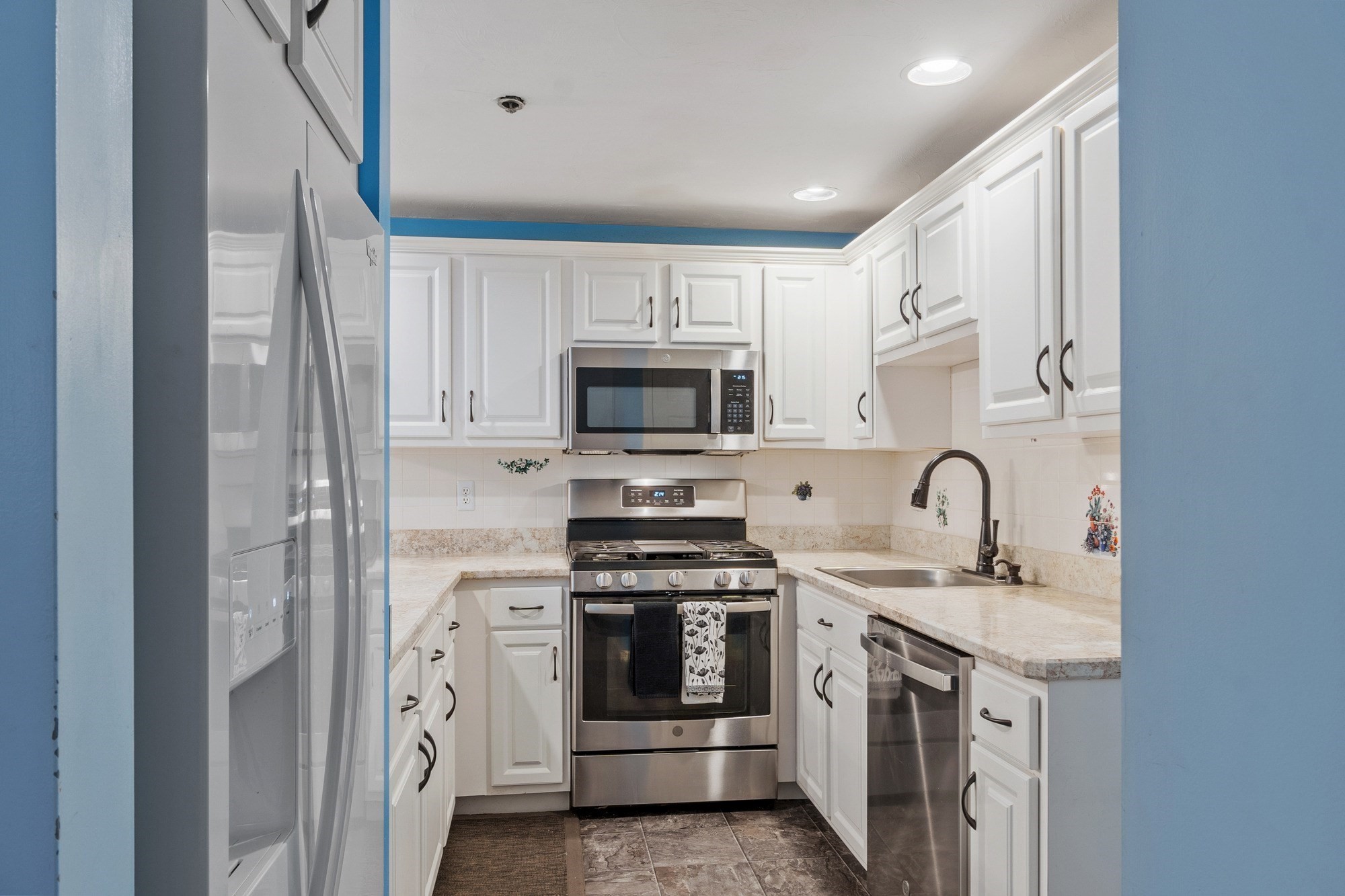 Kitchen with white cabinets, stainless steel appliances, light stone counters, and a deep sink.