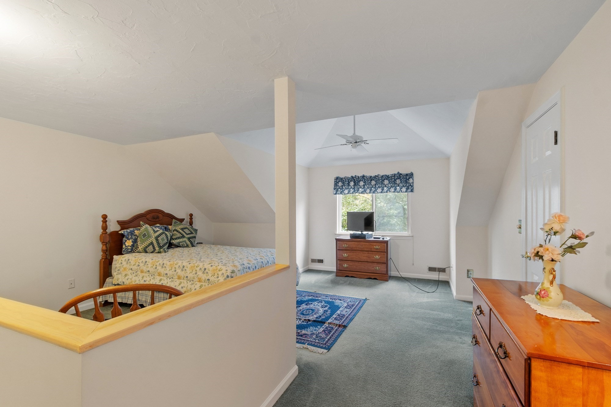 Furnished bedroom with a bed beneath a sloped ceiling and a window at the far end.