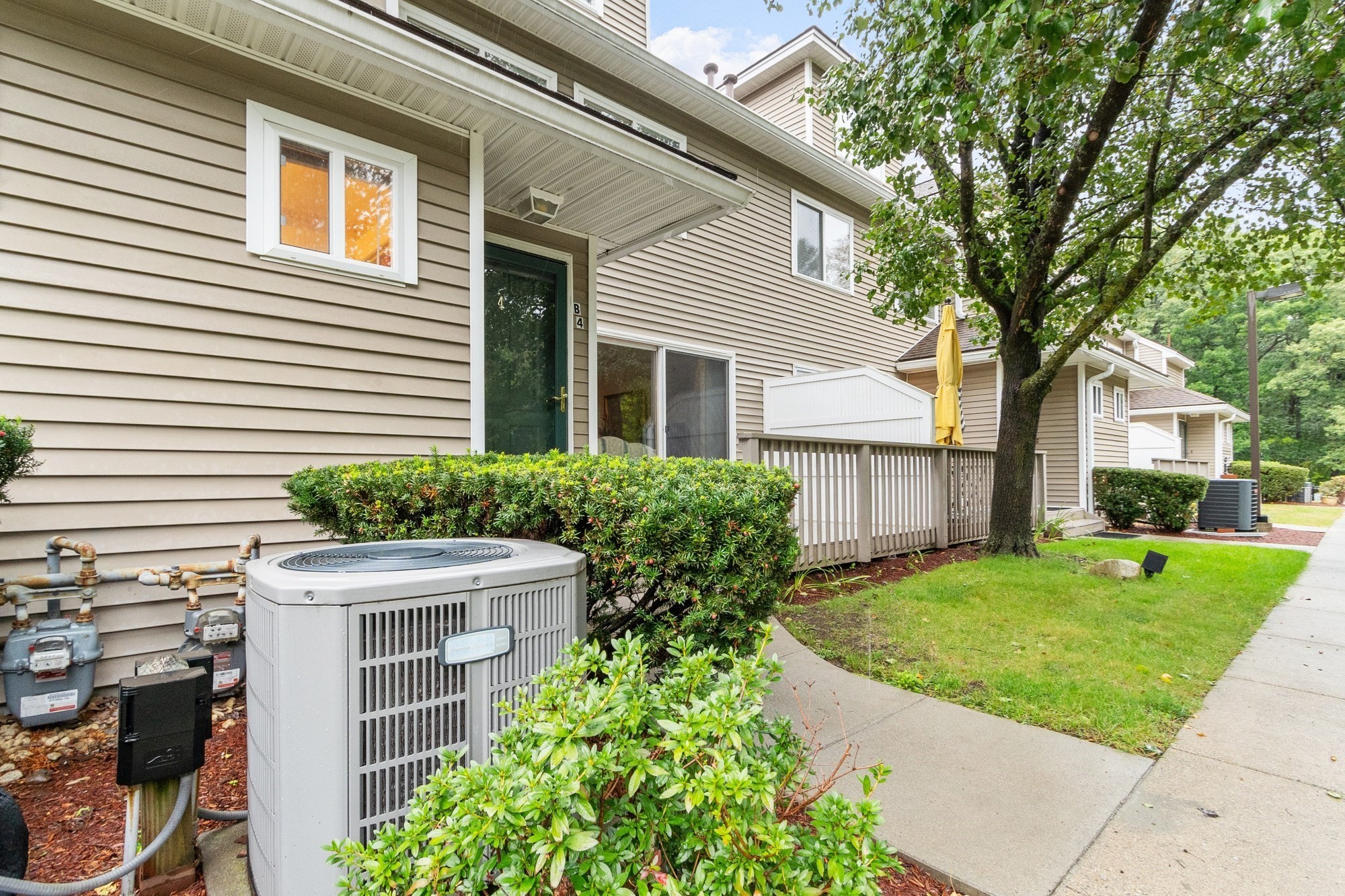 Townhouse entrance with beige siding, a small deck, and landscaped shrubs beside the walkway.