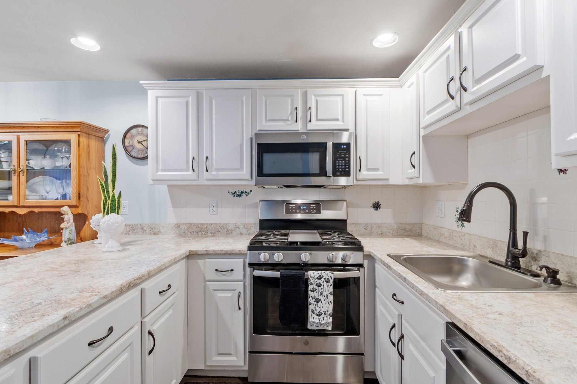 Kitchen with white cabinets, stone counters, stainless steel range, microwave, and a double-basin sink.
