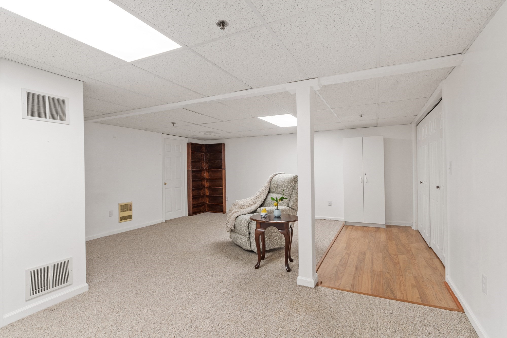 Carpeted room with a patterned armchair, built-in shelves, white closets, and wood-look flooring.