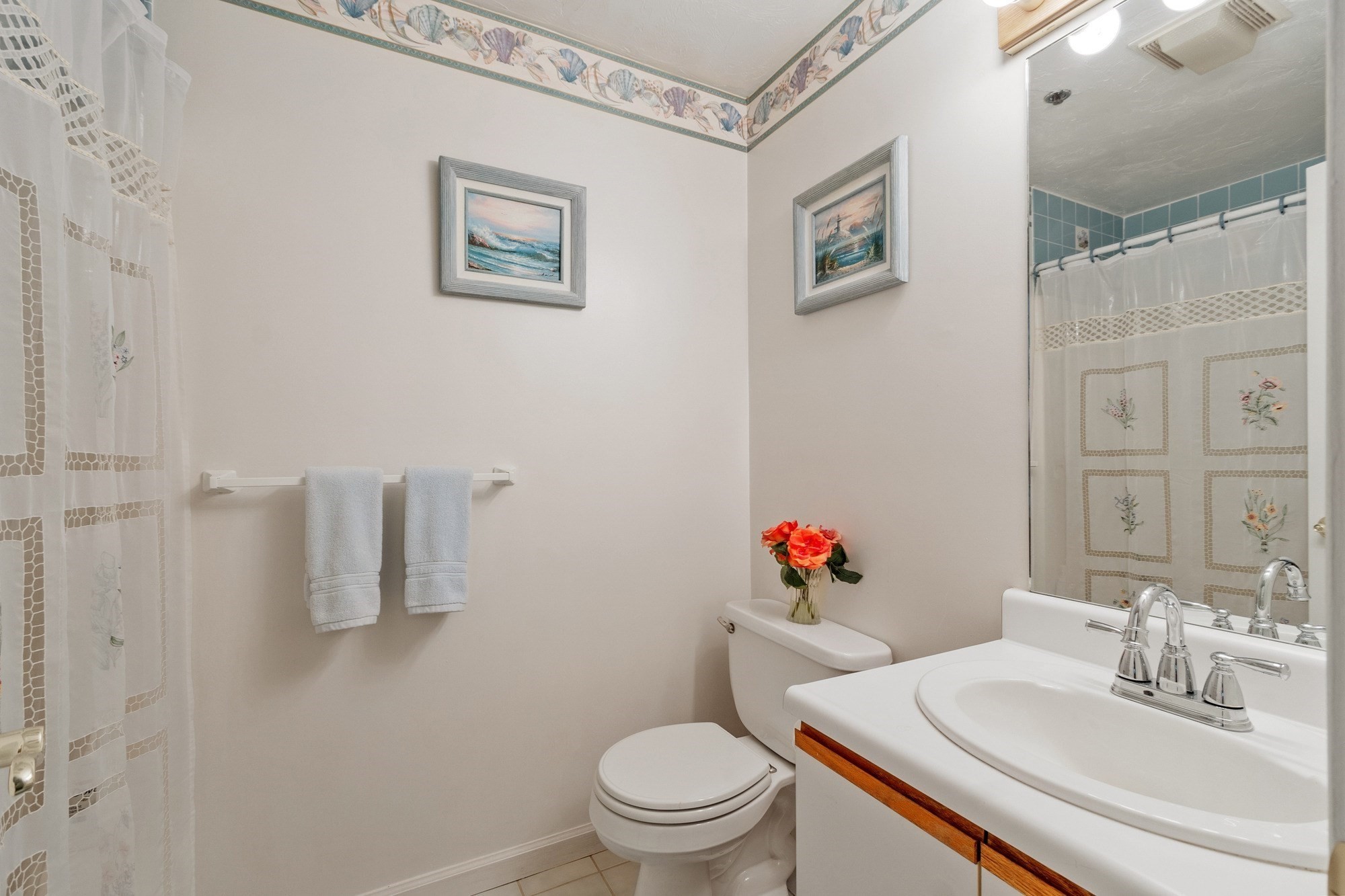 Bathroom with a white vanity, toilet, and floral shower curtain beneath blue shower tiles.