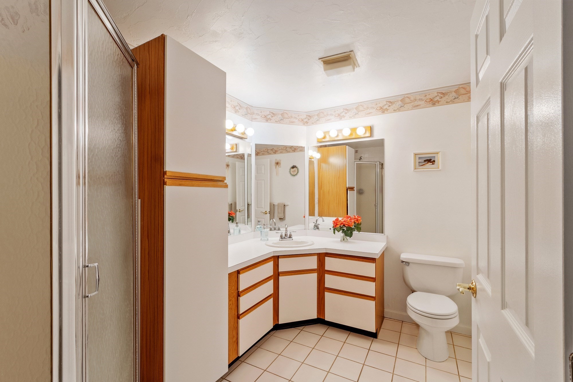 Bathroom with a corner vanity, mirrored wall, glass shower, and beige tiled floor.