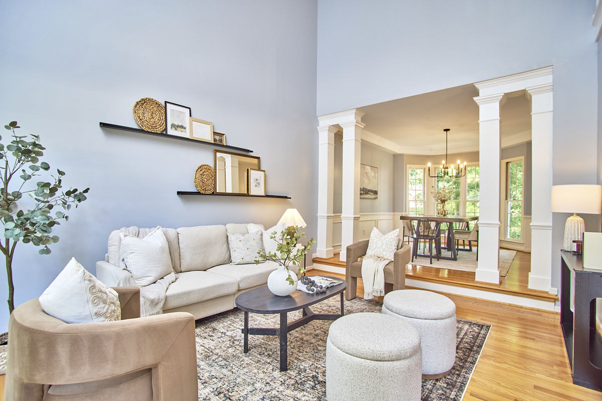 Living room with a cream sofa and ottomans opening to a dining room framed by white columns.