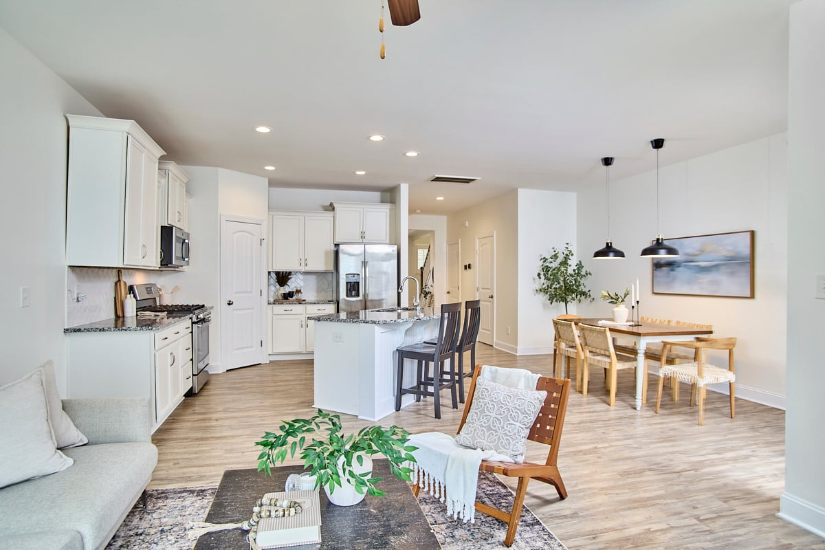 Open-plan kitchen and dining area with a white island, stainless steel appliances, and light wood floors.