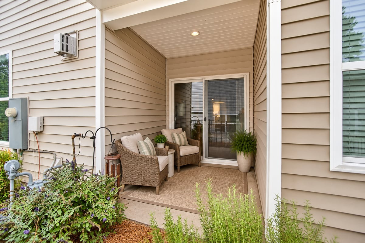 Covered patio with wicker seating, potted plants, and sliding glass doors.